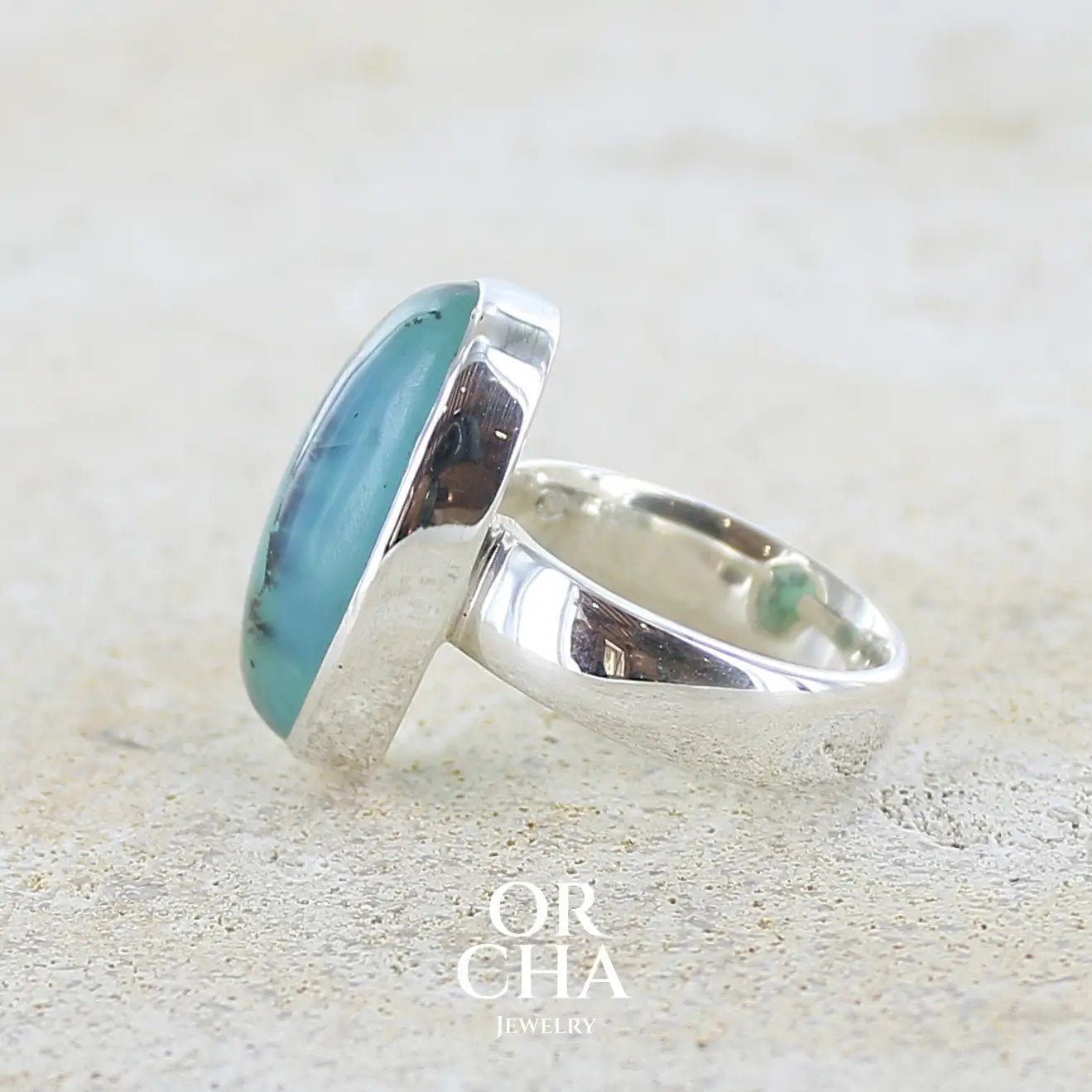 détail du sertissage d'une bague en argent massif, sertie d'un cabochon ovale d'opale bleue du Pérou de couleur bleu foncé à inclusions de dendrites paysages noires et de roche mère jaune. Pierre naturelle opaque et translucide. Bijoux unique réalisé en taille 52 par Orcha jewelry
