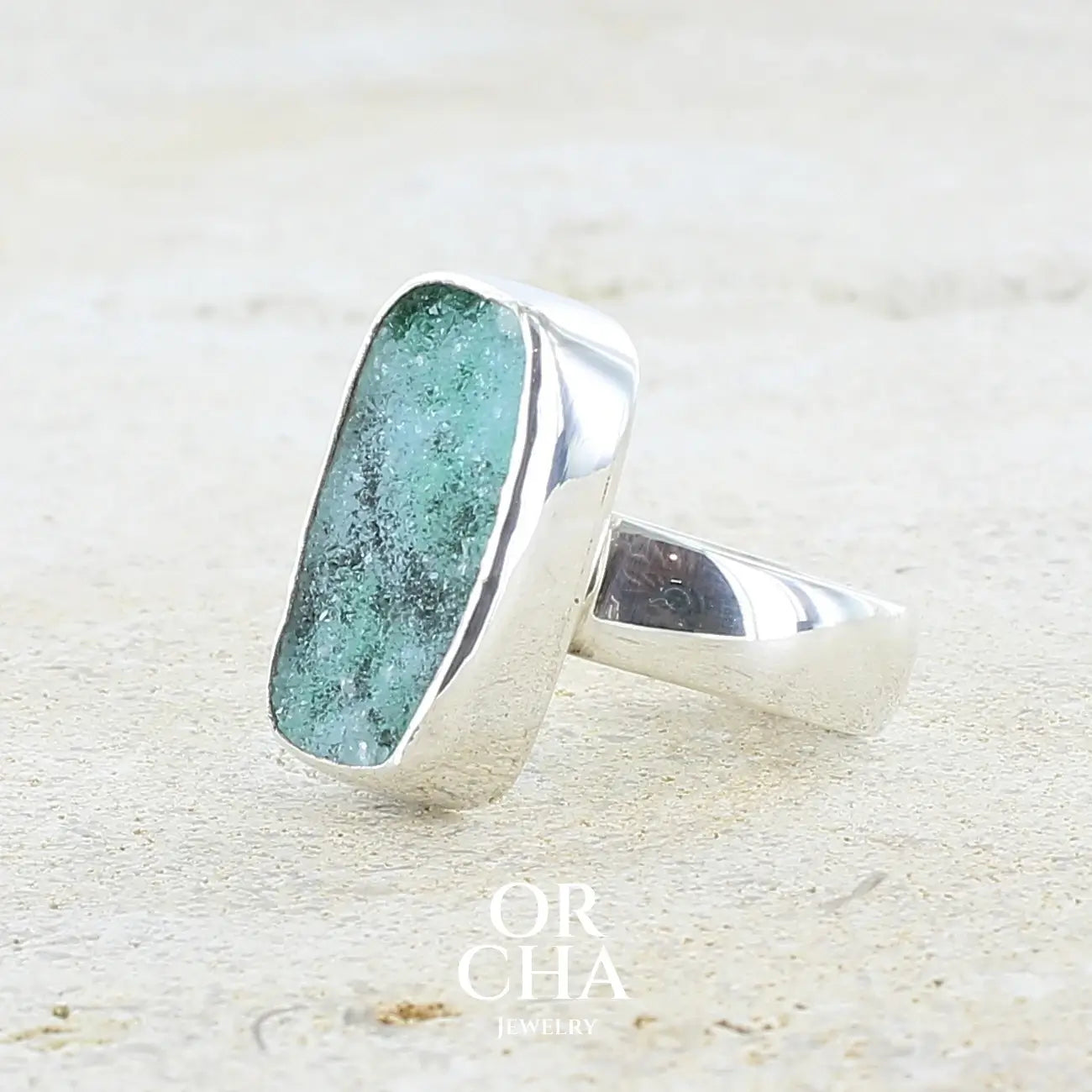détail sertissage d'une bague pour femme en argent massif sertie d'un magnifique gemsilica druzy: chrysocale solidifiée recouverte de fins cristaux de quartz scintillant. Pierre de qualité opaque taillée en tranche de forme rectangulaire. Pierre naturelle originaire de République dominicaine du Congo de couleur turquoise, verte et noire. Taille 56. Bijoux unique, éthique et durable présenté dans un coffret de notre marque, prêt à offrir. Livraison offerte, certificat d'authenticité, service client.