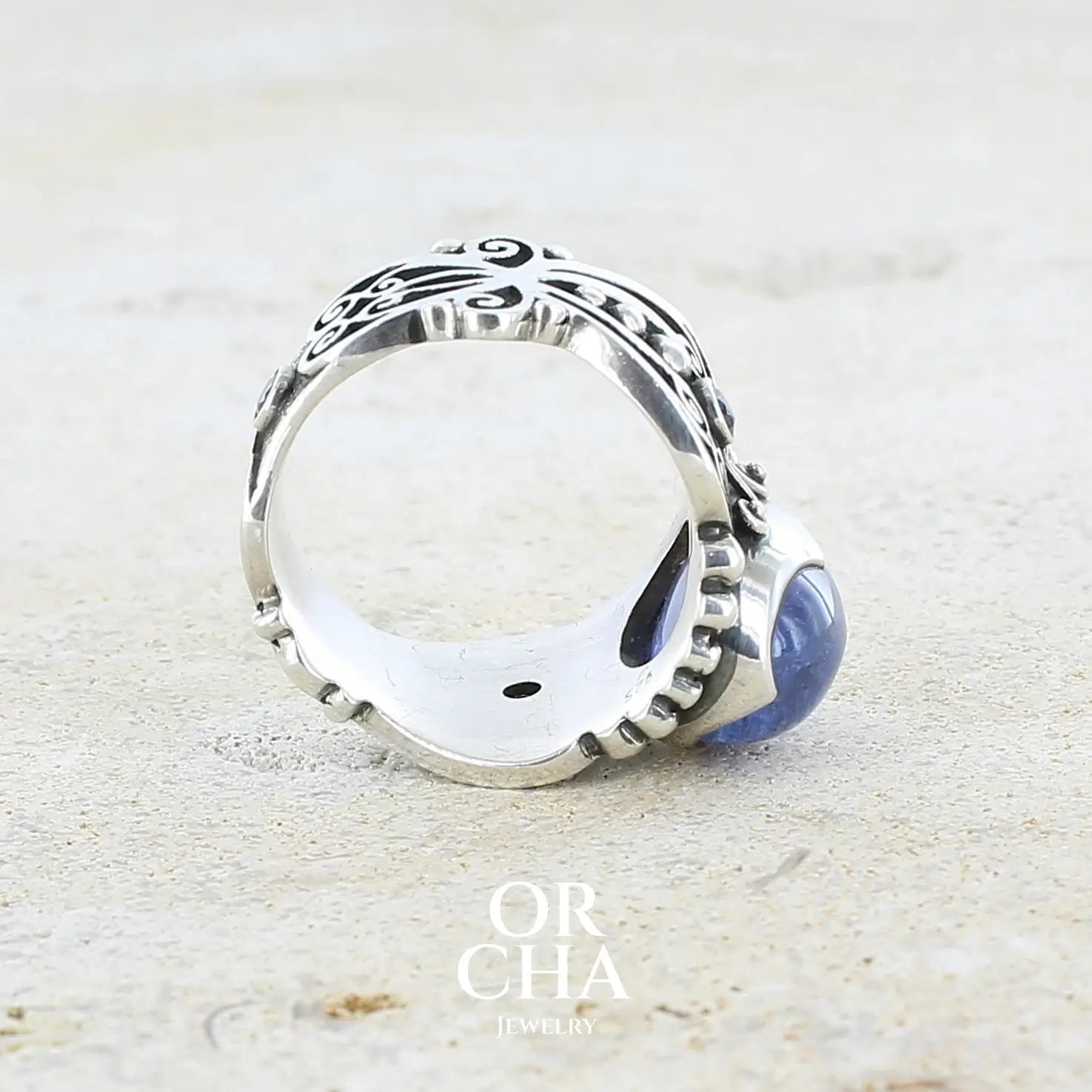 détail de l'epaisseur d'une bague en argent massif sculptées d'entrelacs de style celtique qui illustrent des papillons, sertie d'une Tanzanite. Pierre cabochon de forme ovale, de couleur bleu lavande foncé, de qualité transparente avec inclusions. Taille 56. Bijoux unique, éthique et durable présenté dans un coffret de notre marque, prêt à offrir. Livraison offerte, certificat d'authenticité, service client.
