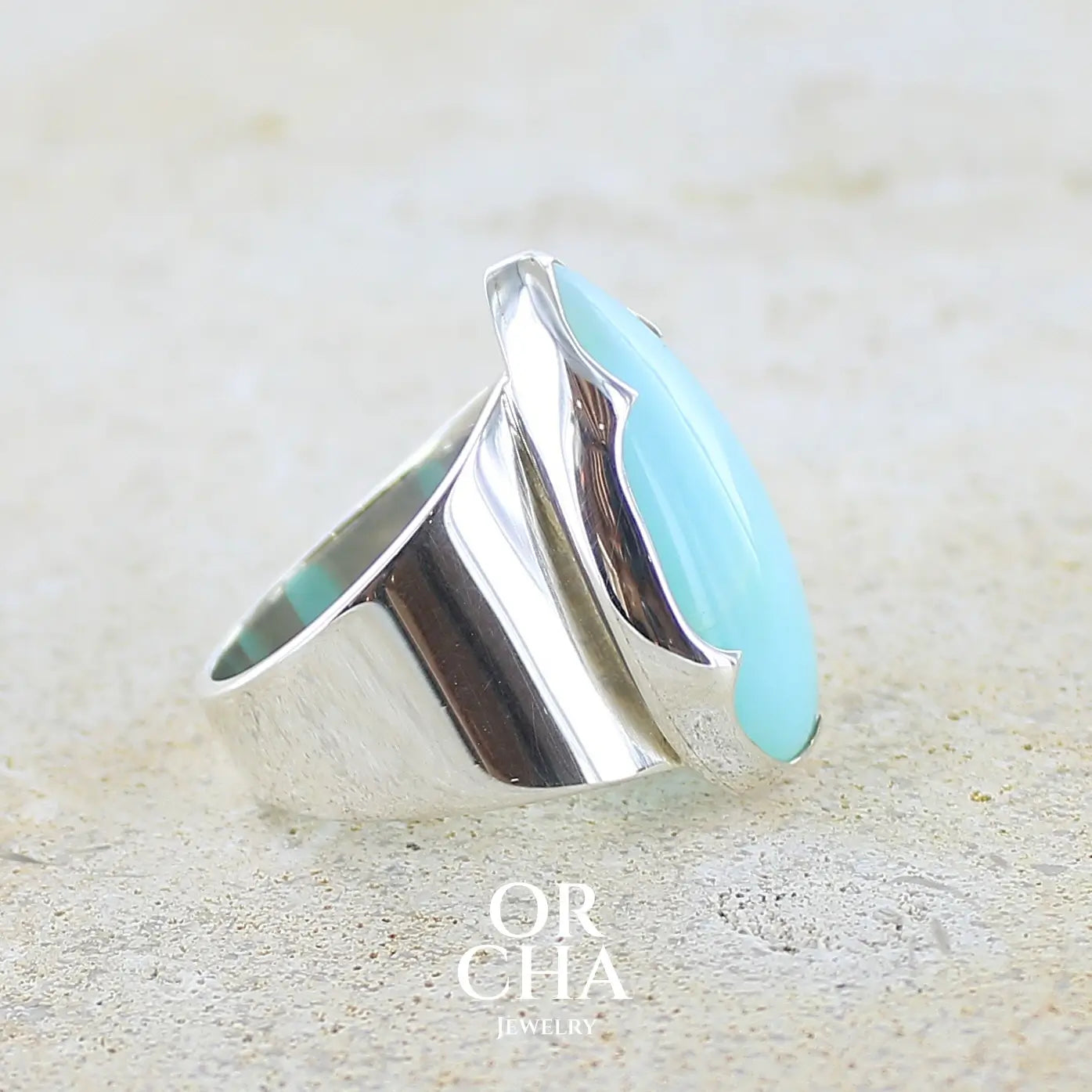 détail du sertissage d'une grande Bague pour femme en argent massif, sertie d'un cabochon d'opale bleue du Pérou de couleur bleu ciel. Pierre taillée en forme de goutte de qualité opaque. Bijou unique réalisé en taille 60 FR.