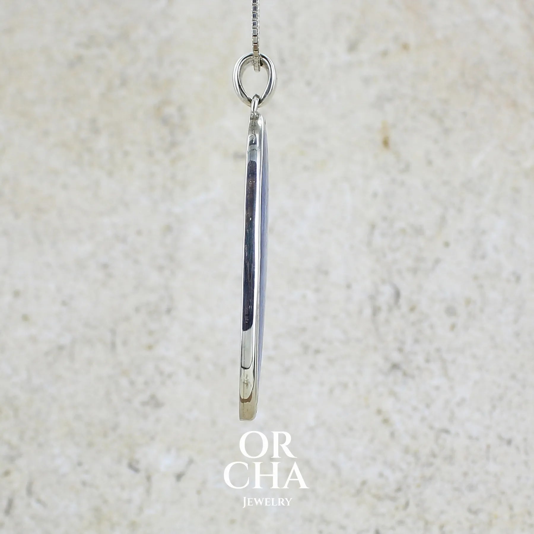 détail du sertissage d'un pendentif en argent massif serti d'un cabochon de cyanite de couleur bleue jeans nacré. Pierre de qualité translucide taillée en forme de goutte inversée comportant des inclusions. Bijoux unique par Orchajewelry