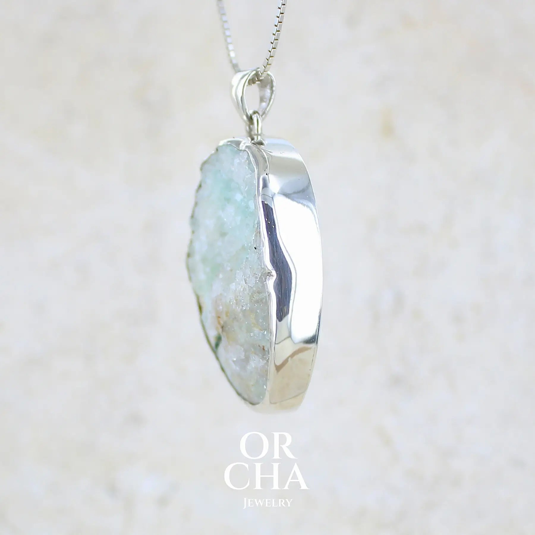 détail du sertissage d'un pendentif en argent massif serti d'un magnifique gemsilica druze: chrysocolle silicifiée recouverte de fins cristaux de quartz scintillant. Pierre de qualité opaque brute de forme ovale. Pierre naturelle originaire du Mexique de couleur verte bleutée claire.

