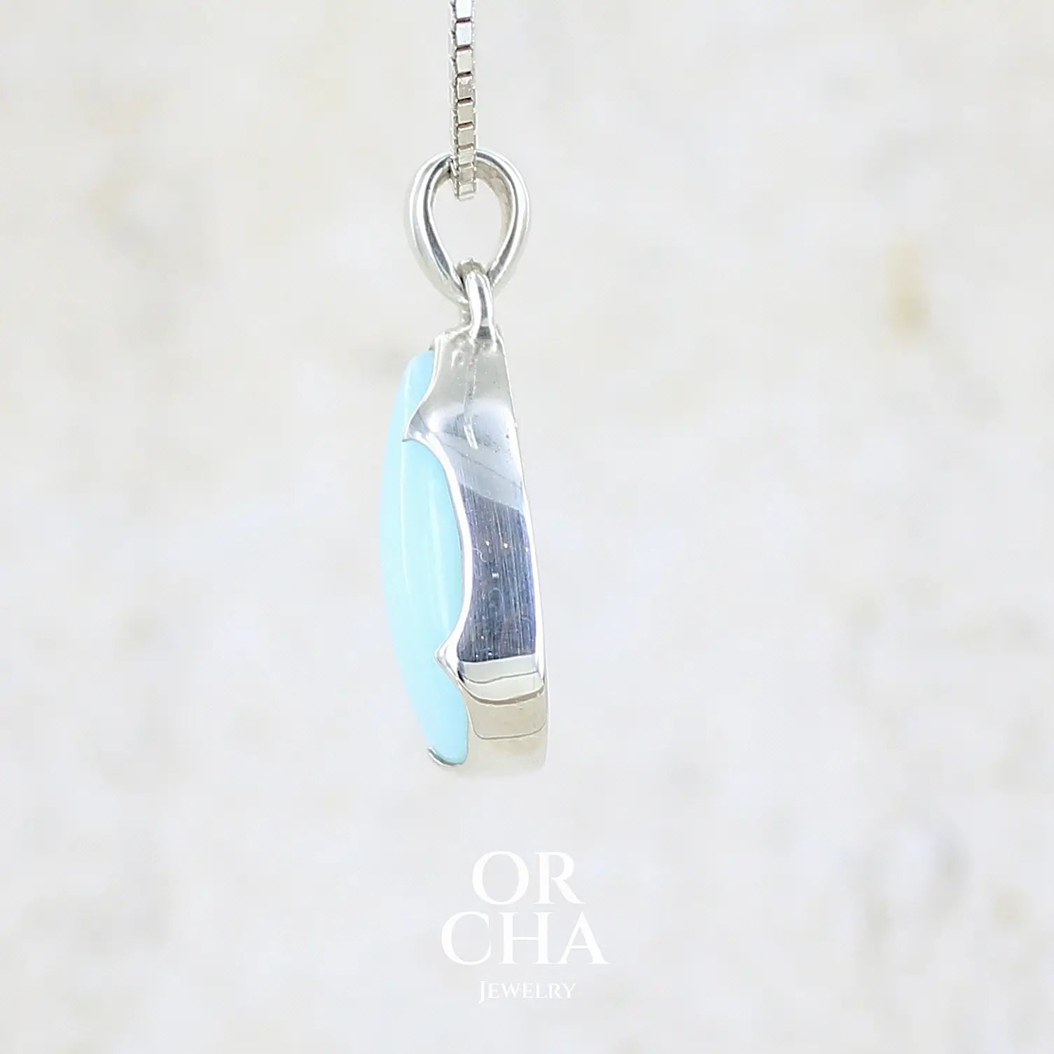 détail texture d'un pendentif pour femme en argent massif, sertie d'un cabochon d'opale bleue du Pérou de couleur bleu ciel clair. Pierre en forme de goutte. Pierre opaque. Bijoux unique, éthique et durable présenté dans un coffret de notre marque, prêt à offrir. Livraison offerte, certificat d'authenticité, service client.