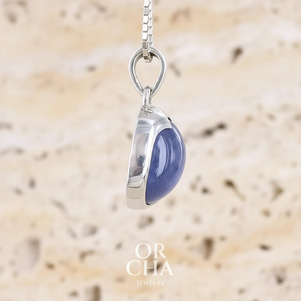 détail du sertissage d'un pendentif pour femme en argent massif serti d'un cabochon de Tanzanite de couleur bleu lavande . Pierre translucide présentant des inclusions. Pierre ayant subit un traitement de chauffe, traitement admis et fréquent en gemmologie pour ce type de pierre . Bijoux unique, éthique et durable présenté dans un coffret de notre marque, prêt à offrir. Livraison offerte, certificat d'authenticité, service client.