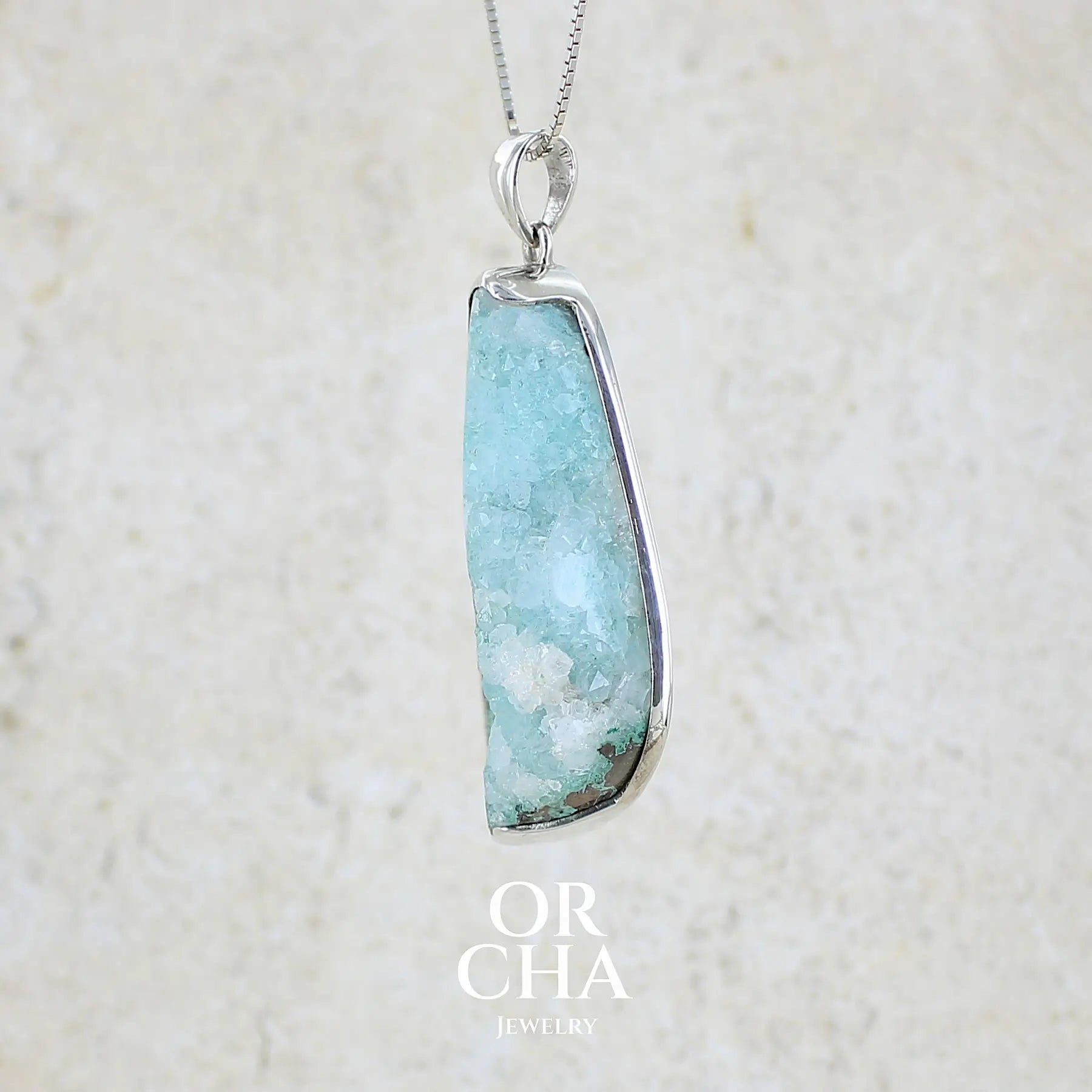 détail du sertissage d'un pendentif en argent massif serti d'un magnifique gemsilica druze: chrysocolle silicifiée recouverte de fins cristaux de quartz scintillant. Pierre de qualité opaque brute en forme de goutte. Pierre naturelle originaire du Mexique de couleur bleue ciel turquoise claire.