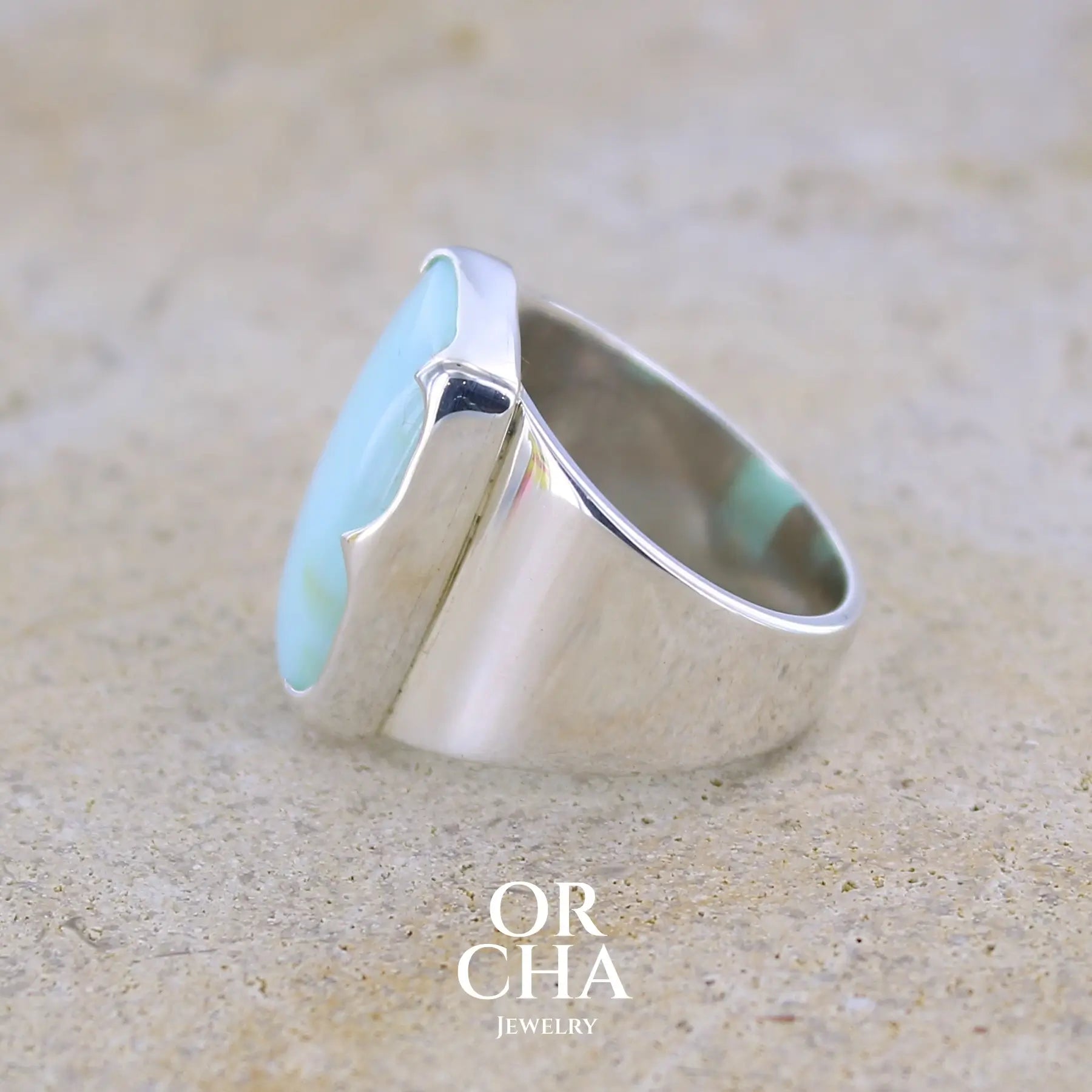 détail texture d'une bague pour femme en argent massif sculptées d'étoiles et autres corps célestes sertie d'une Opale bleue du Pérou. Pierre cabochon en forme de rectangle, pierre naturelle de couleur bleu ciel ciel, bleu turquoise. Pierre naturelle de qualité opaque. Taille 58. Bijoux unique, éthique et durable présenté dans un coffret de notre marque, prêt à offrir. Livraison offerte, certificat d'authenticité, service client.
