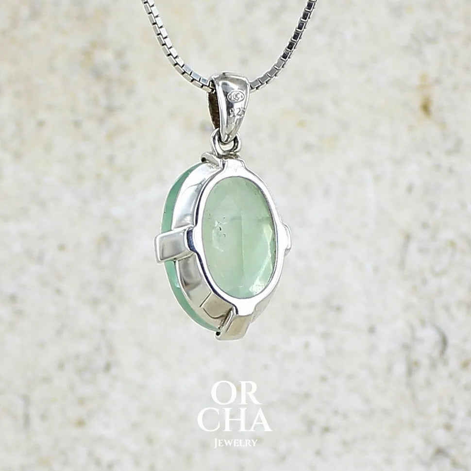 Vue de dos d'un pendentif ovale en argent massif, serti d'un cabochon facetté de préhnite de couleur bleue verte. Pierre de qualité translucide comportant des inclusions. blanches. Bijoux unique par Orcha Jewelry