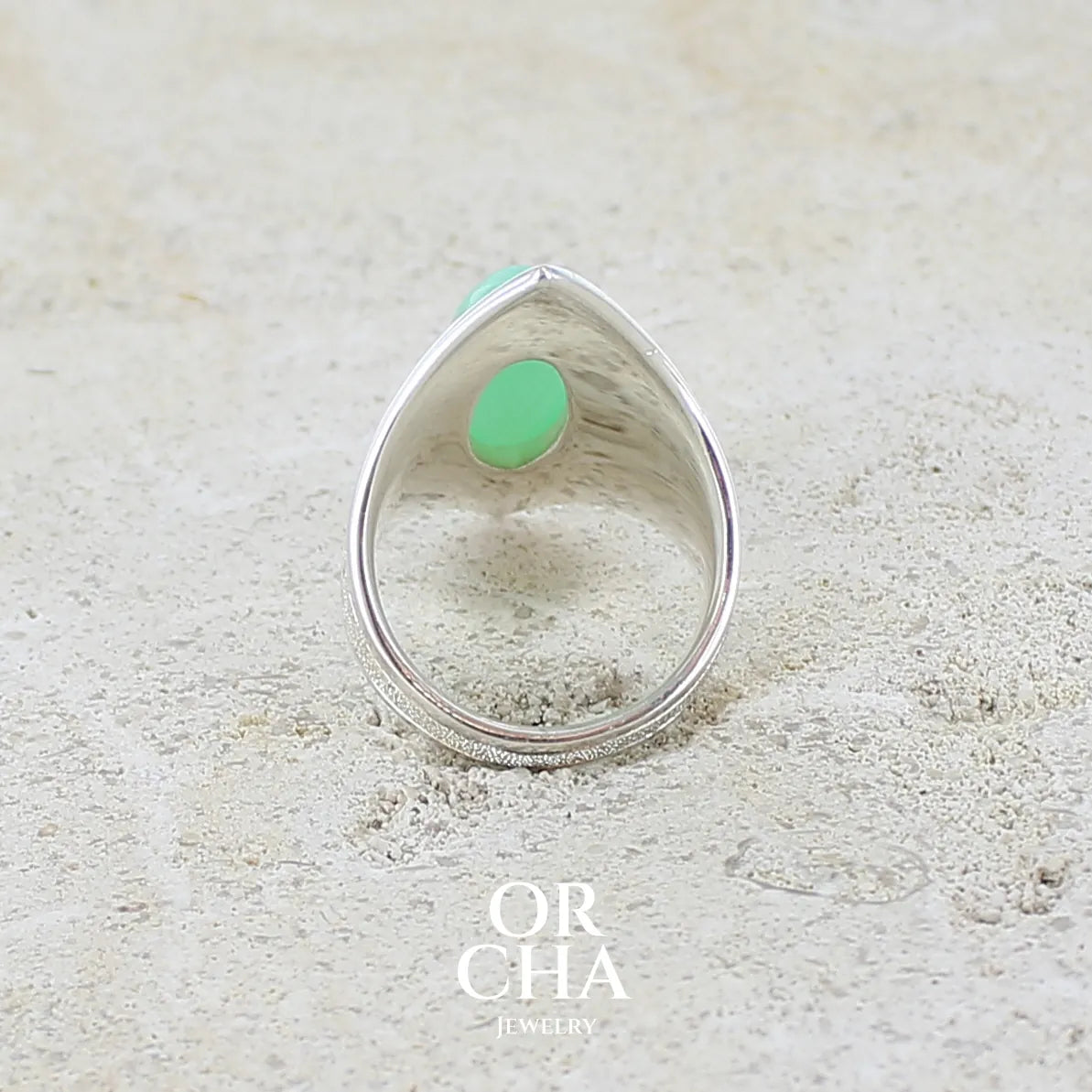 Vue de dos d'une bague marquise pour femme en argent massif sculptées d'étoiles et autres corps célestes sertie d'un cabochon de chrysoprase de couleur verte pastel. Pierre naturelle de qualité translucide taillée en ovale longiligne. Bague unique réalisée en taille 57 par Orcha jewelry