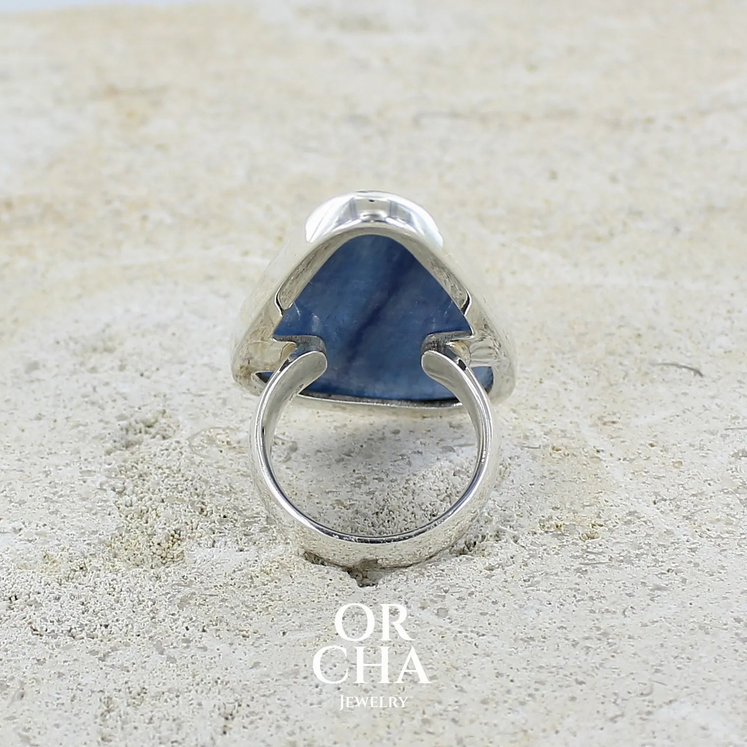 Dos d'une bague longue et imposante pour femme en argent massif, sertie d'un cabochon de cyanite de couleur bleu jean nacré. Pierre taillée en forme de triangle de qualité translucide. Bijou unique réalisée en taille 58 par Orchajewelry