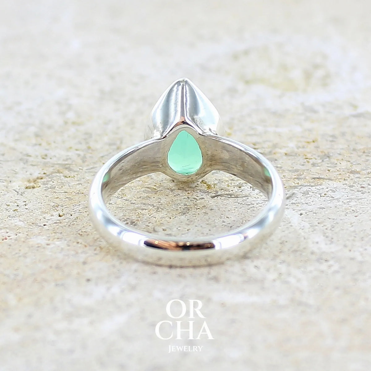 vue de dos d'une bague pour femme en argent massif sertie d'un cabochon de chrysoprase de couleur vert émeraude pastel. Pierre translucide taillée en forme de goutte. Bijou unique réalisé en taille 56 par Orcha Jewelry