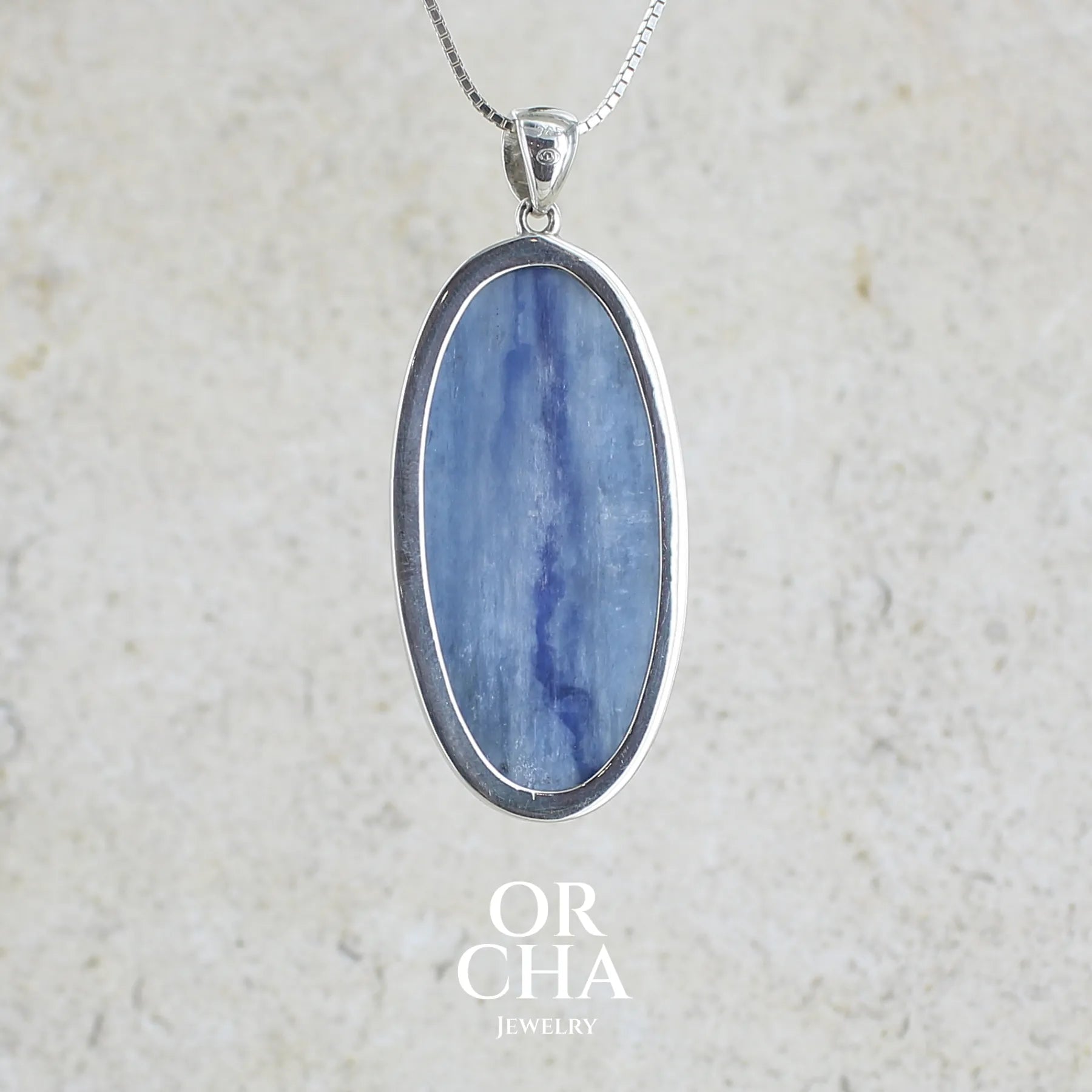 Vue de dos d'un pendentif en argent massif serti d'un cabochon ovale de cyanite de couleur bleue jeans nacré. Pierre de qualité translucide comportant des inclusions.Bijoux unique par Orcha Jewelry