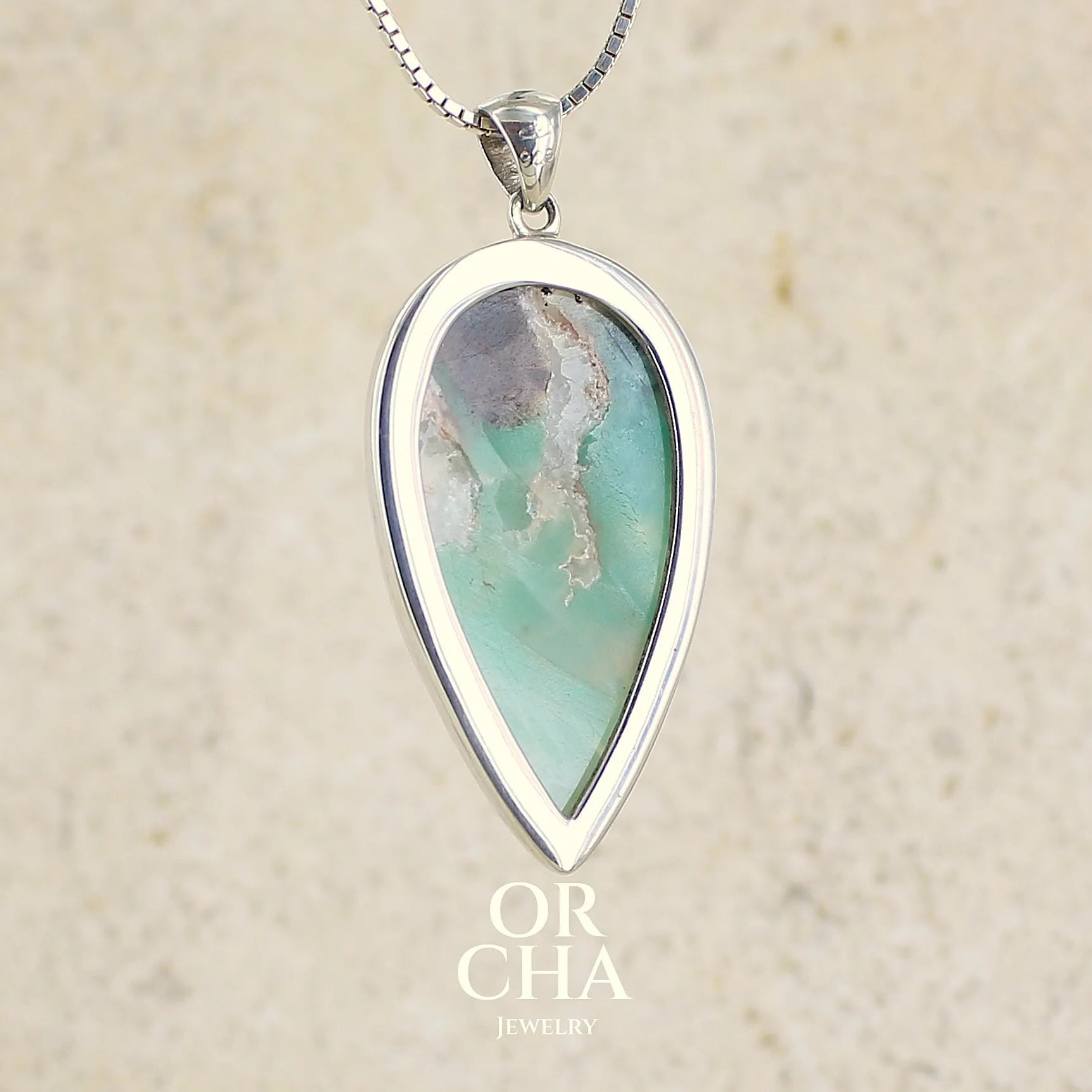 vue de dos d'un pendentif goutte en argent massif, serti d'un cabochon de calcédoine bleue verte  Pierre paysage de qualité translucide et opaque comportant des inclusions. Bijoux unique par Orcha jewelry
