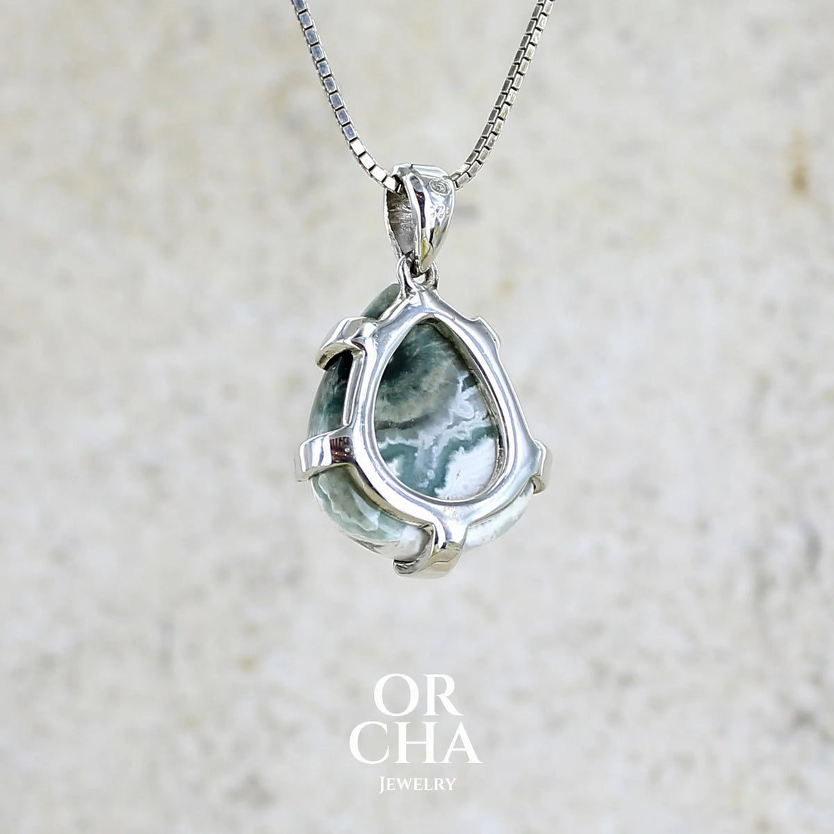 Vue de dos d'un pendentif pour femme en argent massif sertie d'un cabochon de jaspe océan de couleur nuancée de kaki et crème. Pierre opaque taillée en forme de goutte. Bijou unique par Orchajewelry

