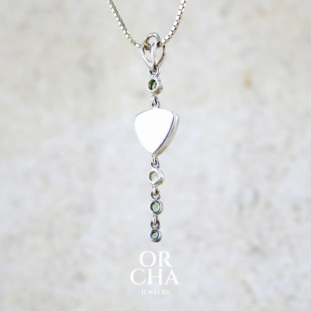 Vue de dos d'un pendentif pour femme en argent massif sertie d'un cabochon triangulaire de Préhnite ainsi que de petites tourmalines vertes formant une cascade colorée vert pastel lumineux. Pierre transparente à inclusions. Bijou unique réalisé par Orchajewelry