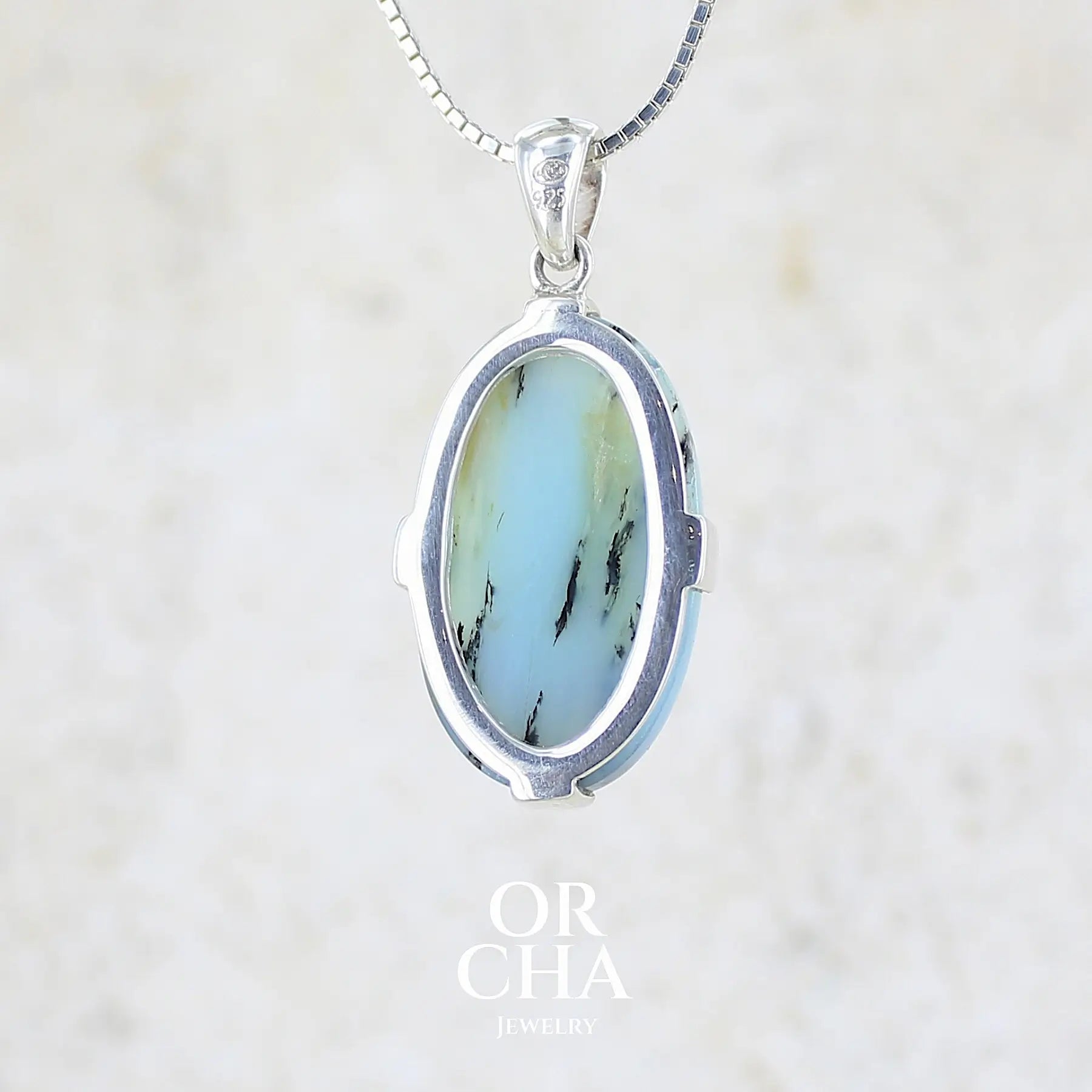 vue de dos d'un pendentif pour femme et homme en argent massif, sertie d'un cabochon d'opale bleue du Pérou de couleur verte bleutée. Pierre en forme de goutte inversée. Pierre opaque et translucide. Bijoux unique, éthique et durable présenté dans un coffret de notre marque, prêt à offrir. Livraison offerte, certificat d'authenticité, service client.
