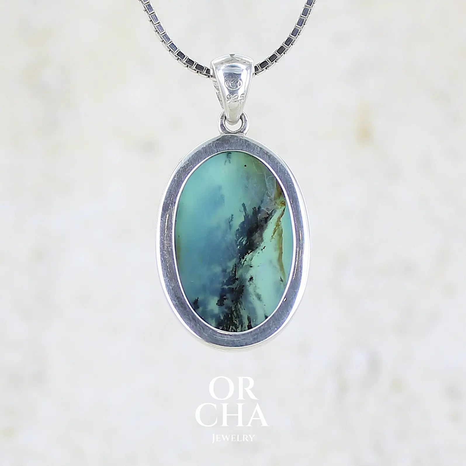vue de dos d'un pendentif en argent massif, sertie d'un cabochon ovale d'opale bleue du Pérou de couleur bleu laiteux foncé à inclusions de dendrites paysages noires et de roche mère marron. Pierre opaque et translucide. Bijoux unique, éthique et durable présenté dans un coffret de notre marque, prêt à offrir. Livraison offerte, certificat d'authenticité, service client.