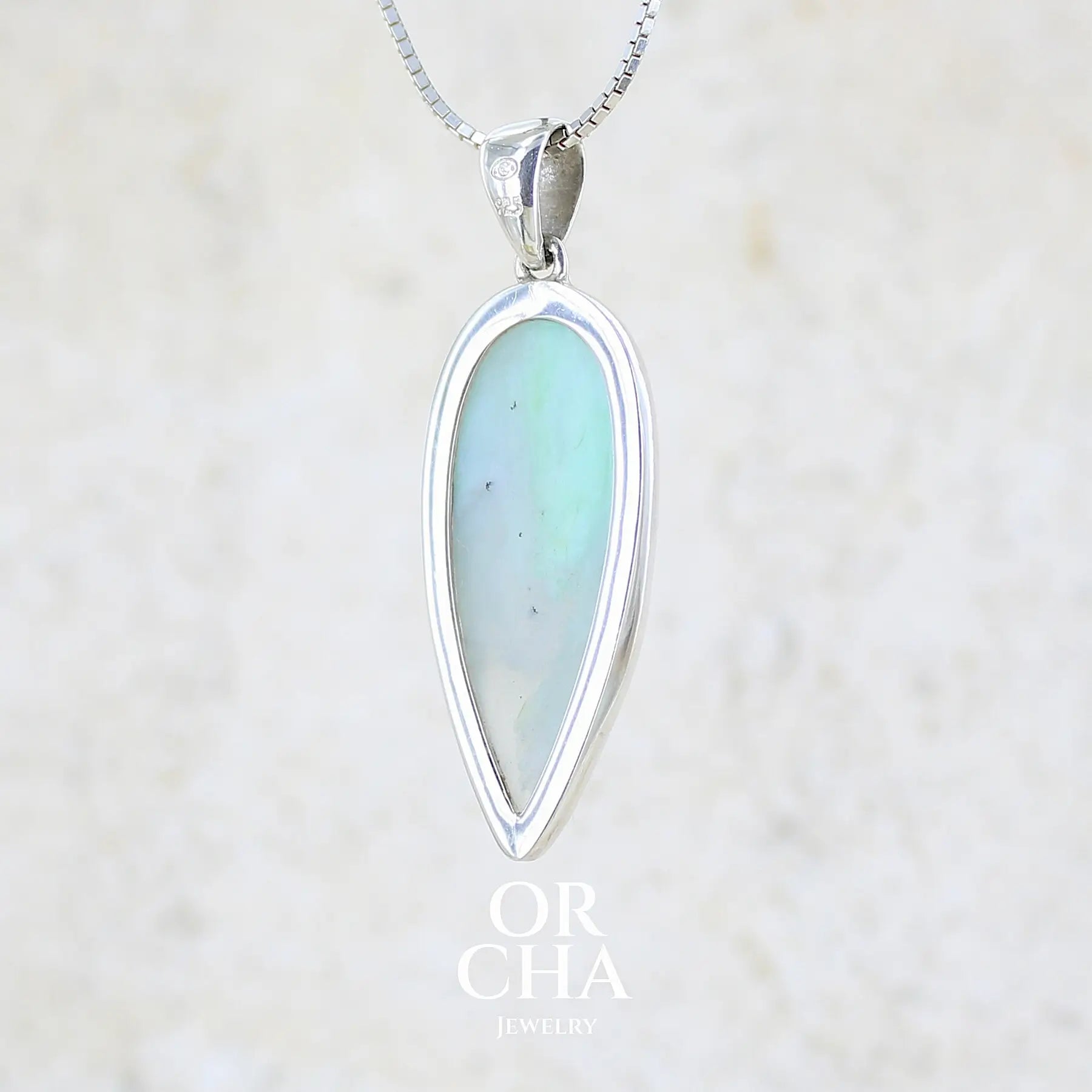 vue de dos d'un pendentif pour femme et homme en argent massif, sertie d'un cabochon d'opale bleue du Pérou de couleur verte bleutée. Pierre en forme de goutte inversée. Pierre opaque et translucide. Bijoux unique, éthique et durable présenté dans un coffret de notre marque, prêt à offrir. Livraison offerte, certificat d'authenticité, service client.
