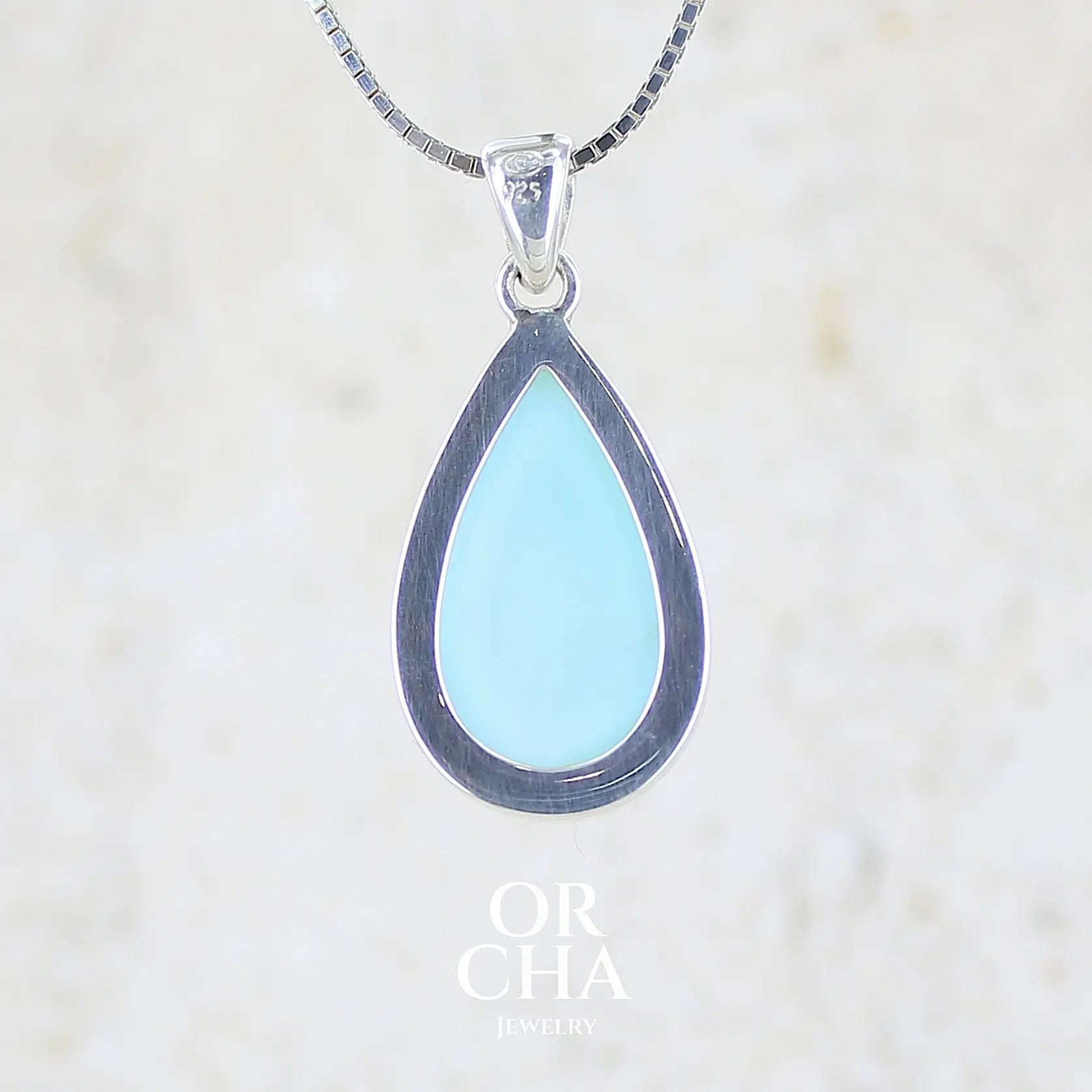 vue de dos d'un pendentif pour femme en argent massif, sertie d'un cabochon d'opale bleue du Pérou de couleur bleu ciel clair. Pierre en forme de goutte. Pierre opaque. Bijoux unique, éthique et durable présenté dans un coffret de notre marque, prêt à offrir. Livraison offerte, certificat d'authenticité, service client.