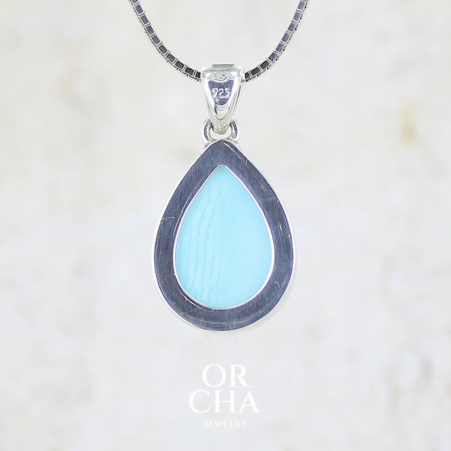 vue de dos d'un pendentif pour femme en argent massif, sertie d'un cabochon d'opale bleue du Pérou de couleur bleu ciel clair. Pierre en forme de goutte. Pierre opaque. Bijoux unique, éthique et durable présenté dans un coffret de notre marque, prêt à offrir. Livraison offerte, certificat d'authenticité, service client.