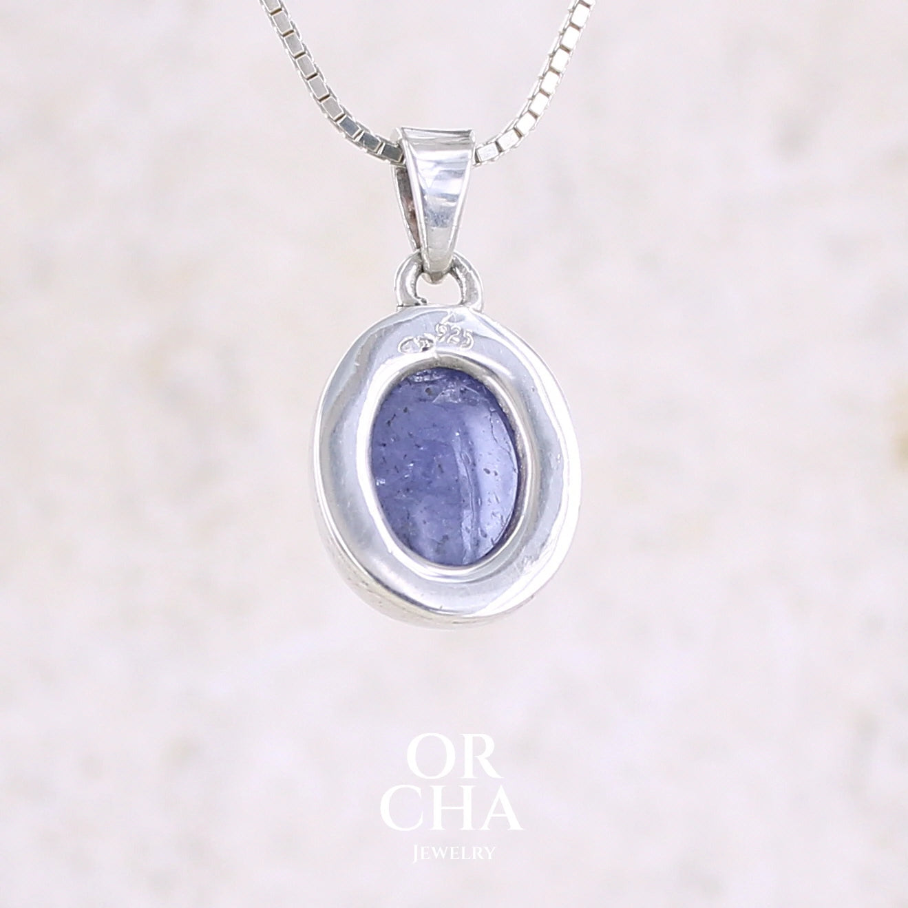 vue de dos d'un pendentif pour femme en argent massif serti d'un cabochon de Tanzanite de couleur bleu lavande . Pierre translucide présentant des inclusions. Pierre ayant subit un traitement de chauffe, traitement admis et fréquent en gemmologie pour ce type de pierre . Bijoux unique, éthique et durable présenté dans un coffret de notre marque, prêt à offrir. Livraison offerte, certificat d'authenticité, service client.