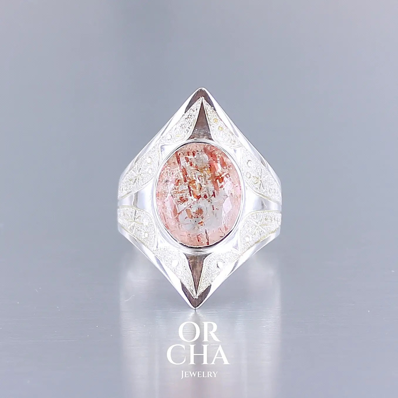 Bague pour femme en argent massif sculptées d'étoiles et autres corps célestes sertie d'une pierre de soleil aux nuances orangées rouges scintillantes. Pierre naturelle, facettée de forme ovale, de qualité transparente pierre transparente avec inclusions scintillantes d'hématites. Taille 59. Bijoux unique, éthique et durable présenté dans un coffret de notre marque, prêt à offrir. Livraison offerte, certificat d'authenticité, service client.