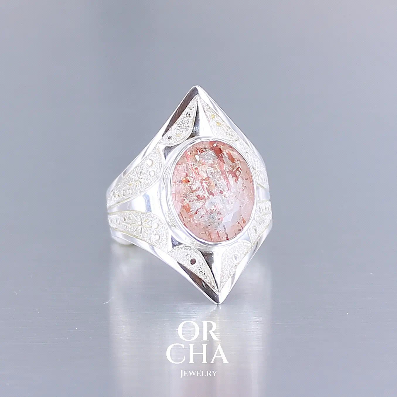 Photo de profil d'une bague pour femme en argent massif sculptées d'étoiles et autres corps célestes sertie d'une pierre de soleil aux nuances orangées rouges scintillantes. Pierre naturelle, facettée de forme ovale, de qualité transparente pierre transparente avec inclusions scintillantes d'hématites. Taille 59. Bijoux unique, éthique et durable présenté dans un coffret de notre marque, prêt à offrir. Livraison offerte, certificat d'authenticité, service client.