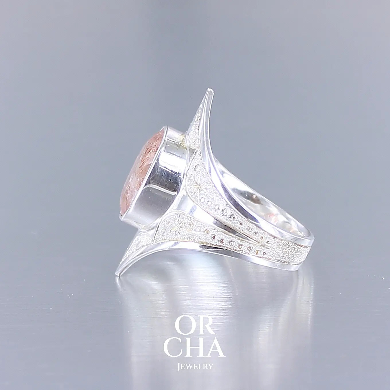 Photo de profil d'une bague pour femme en argent massif sculptées d'étoiles et autres corps célestes sertie d'une pierre de soleil aux nuances orangées rouges scintillantes. Pierre naturelle, facettée de forme ovale, de qualité transparente pierre transparente avec inclusions scintillantes d'hématites. Taille 59. Bijoux unique, éthique et durable présenté dans un coffret de notre marque, prêt à offrir. Livraison offerte, certificat d'authenticité, service client.