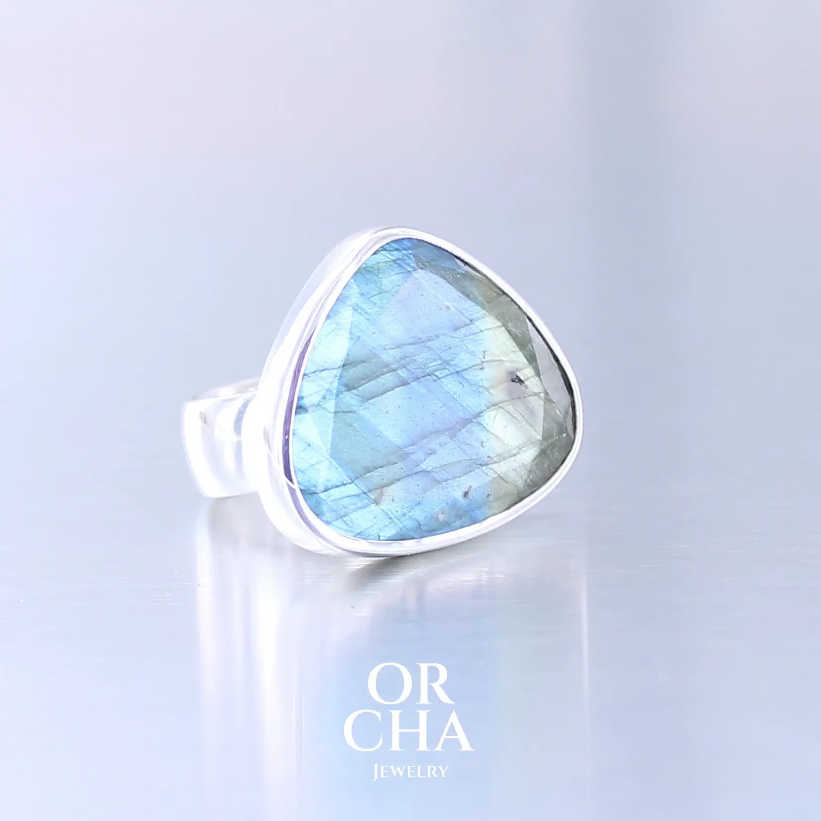 Bague pour femme en argent massif sertie d'une labradorite aux reflets bleus et verts selon la lumière. Pierre facettée naturelle translucide présentant des inclusions fréquents sur ce type de pierre. Taille 56. Bijoux unique, éthique et durable présenté dans un coffret de notre marque, prêt à offrir. Livraison offerte, certificat d'authenticité, service client.