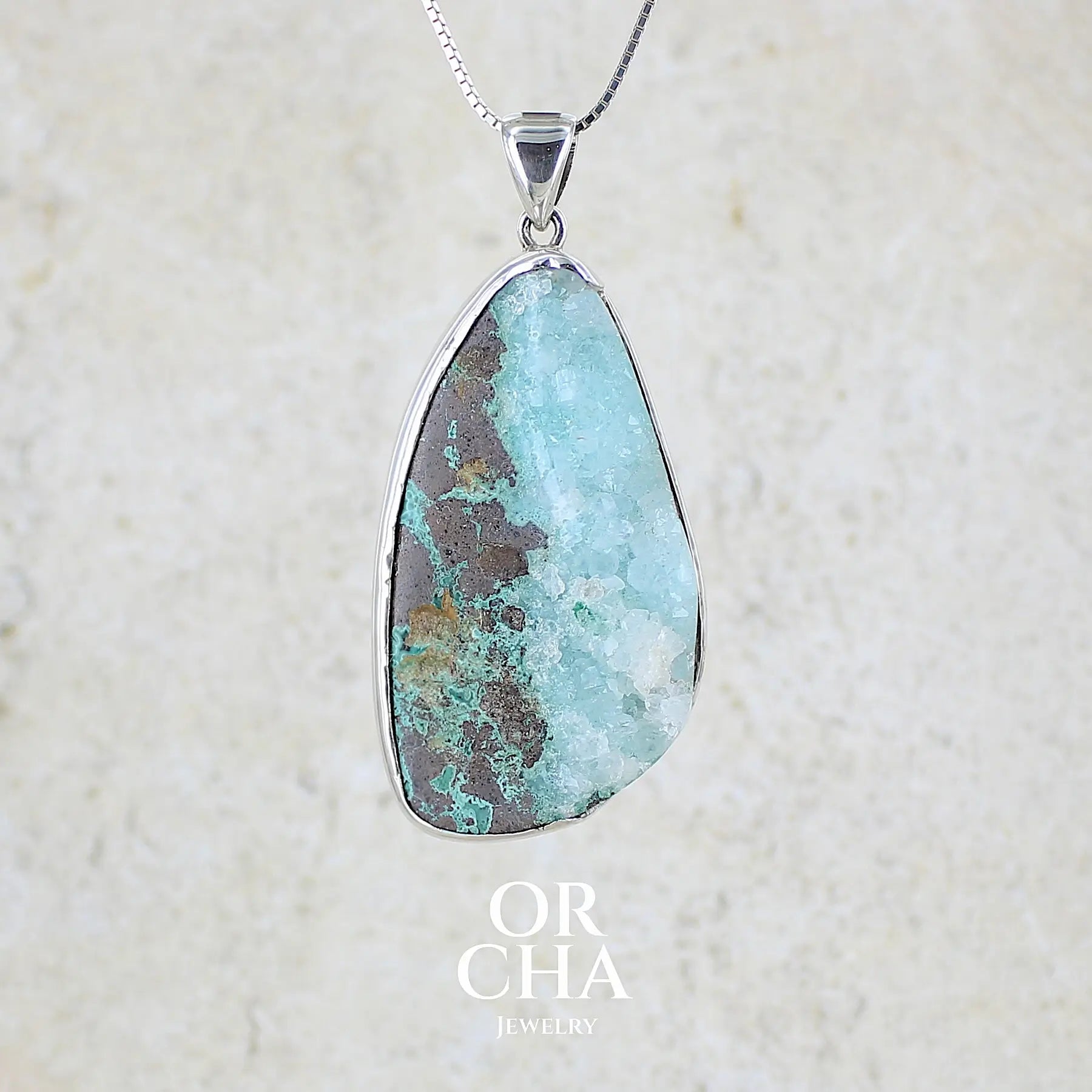 Pendentif en argent massif serti d'un magnifique gemsilica druze: chrysocolle silicifiée recouverte de fins cristaux de quartz scintillant. Pierre de qualité opaque brute en forme de goutte. Pierre naturelle originaire du Mexique de couleur bleue ciel turquoise claire.
