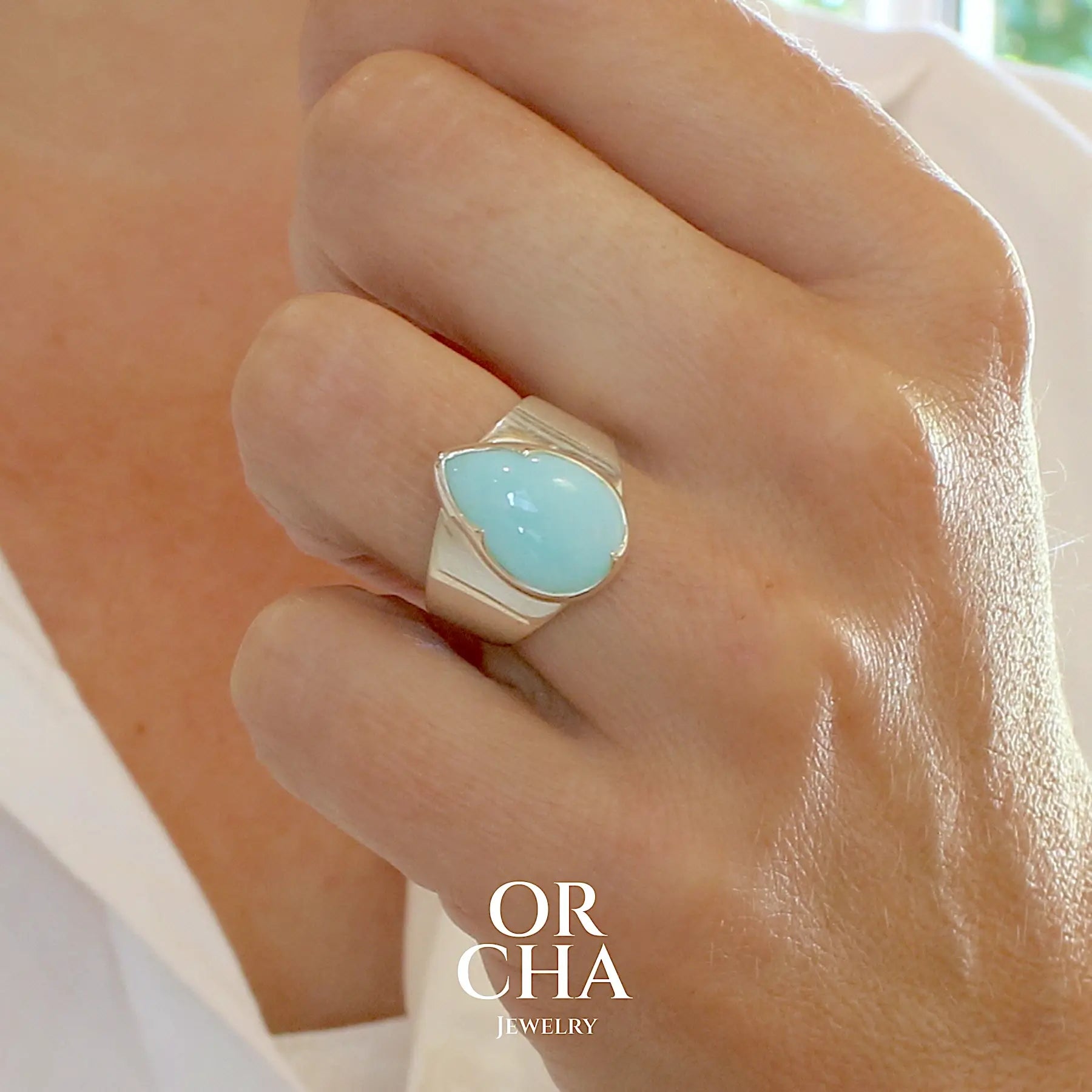 Photo portée d'une bague pour femme en argent massif, sertie d'un cabochon d'opale bleue du Pérou de couleur bleu ciel. Pierre taillée en forme de goutte de qualité opaque. Bijou unique de taille 56
