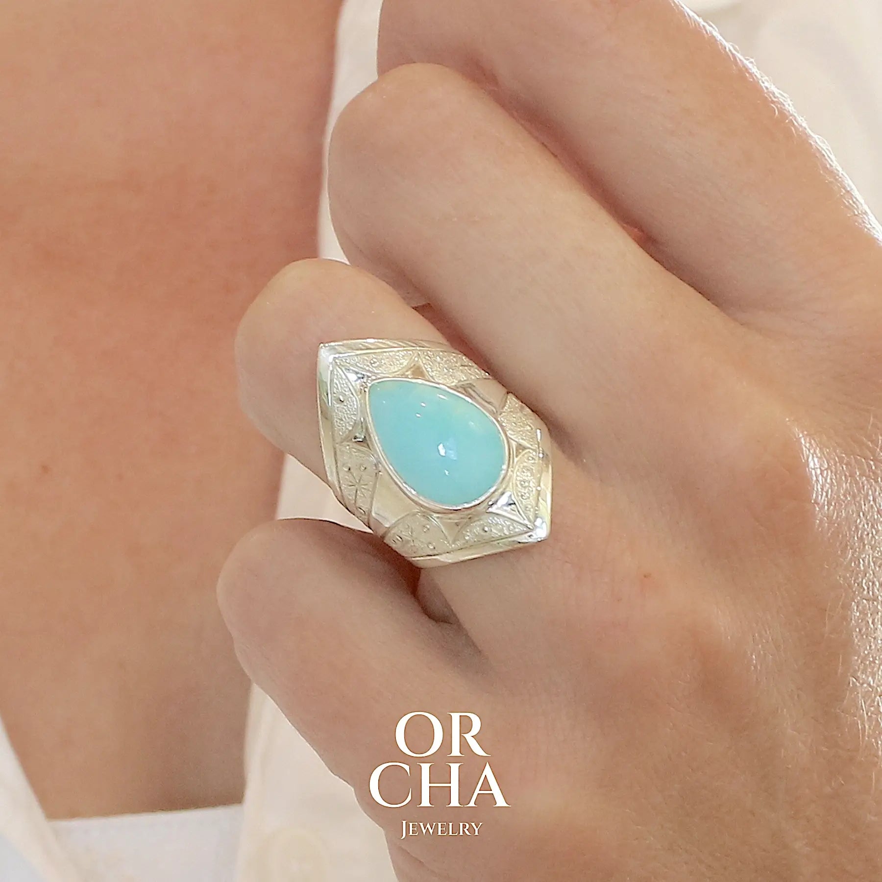 photo sur modèle d'une grande Bague pour femme en argent massif, sertie d'un cabochon d'opale bleue du Pérou de couleur bleu ciel turquoise. Pierre taillée en forme de goutte. de qualité opaque. bijou unique réalisé en taille 52.  