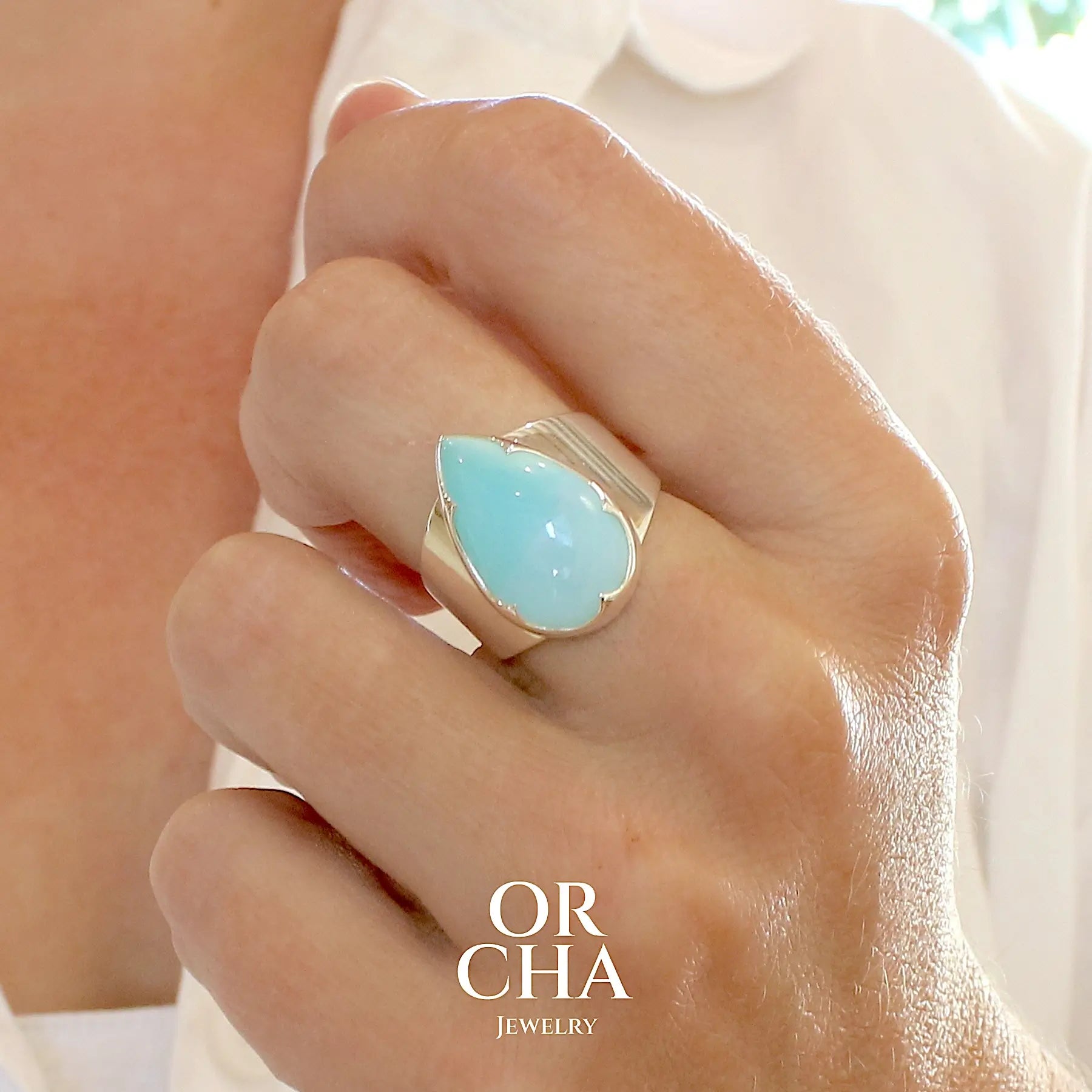photo portée d'une bague pour femme en argent massif, sertie d'un cabochon d'opale bleue du Pérou de couleur bleu ciel. Pierre taillée en forme de goutte de qualité opaque. Bijou unique réalisé en taille 58. 