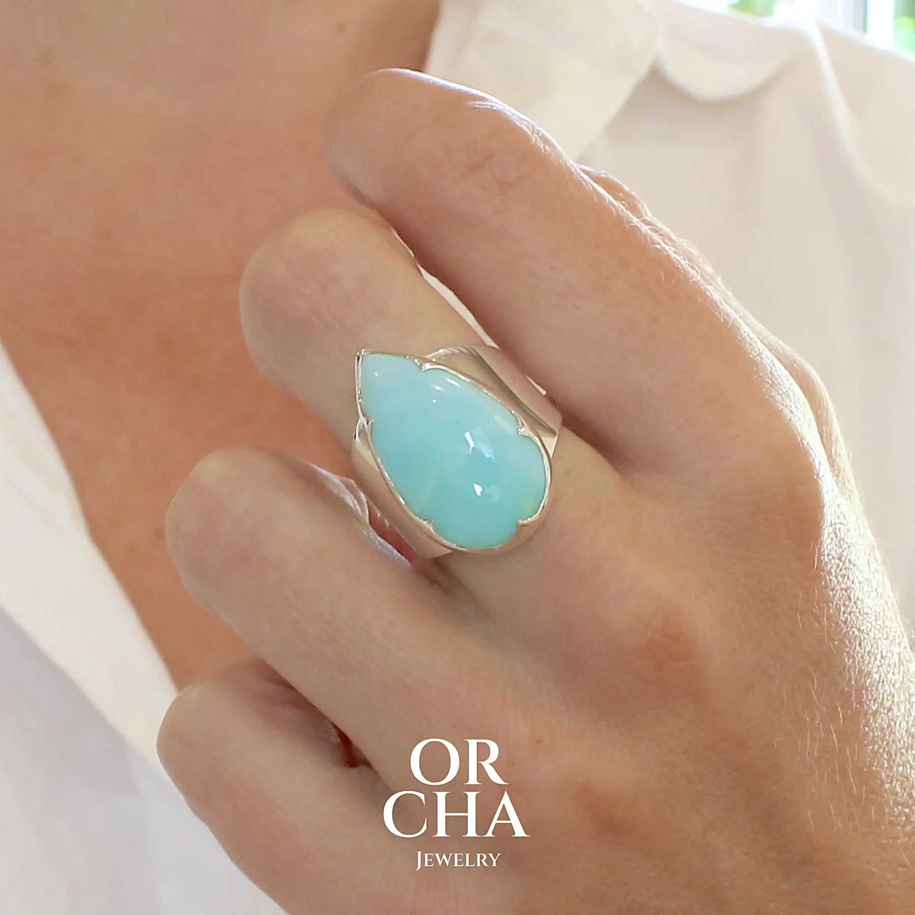 Photo sur modèle d'une grande Bague pour femme en argent massif, sertie d'un cabochon d'opale bleue du Pérou de couleur bleu ciel. Pierre taillée en forme de goutte de qualité opaque. Bijou unique réalisé en taille 60 FR.