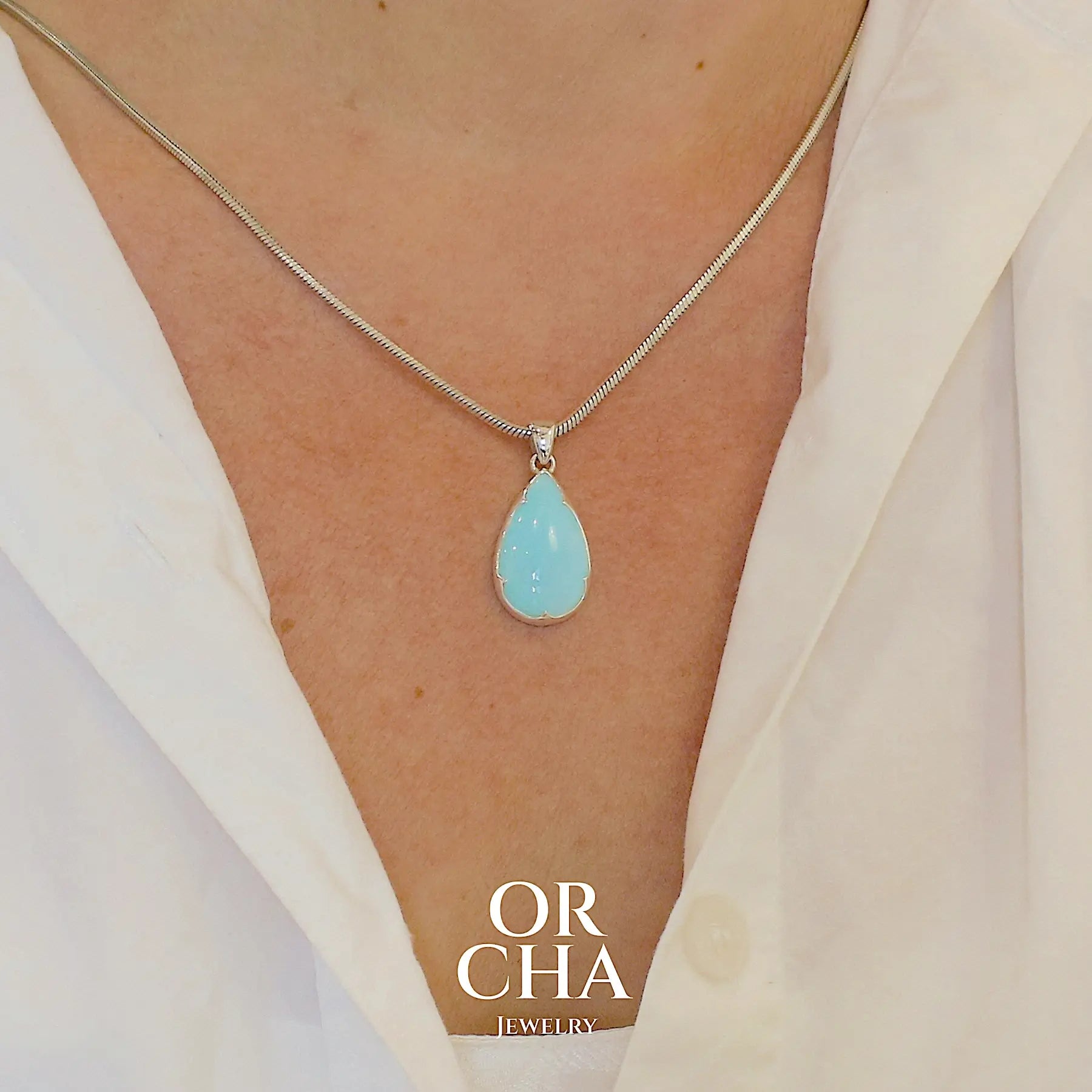 photo sur model d'un pendentif pour femme en argent massif, sertie d'un cabochon d'opale bleue du Pérou de couleur bleu ciel clair. Pierre en forme de goutte. Pierre opaque. Bijoux unique, éthique et durable présenté dans un coffret de notre marque, prêt à offrir. Livraison offerte, certificat d'authenticité, service client.