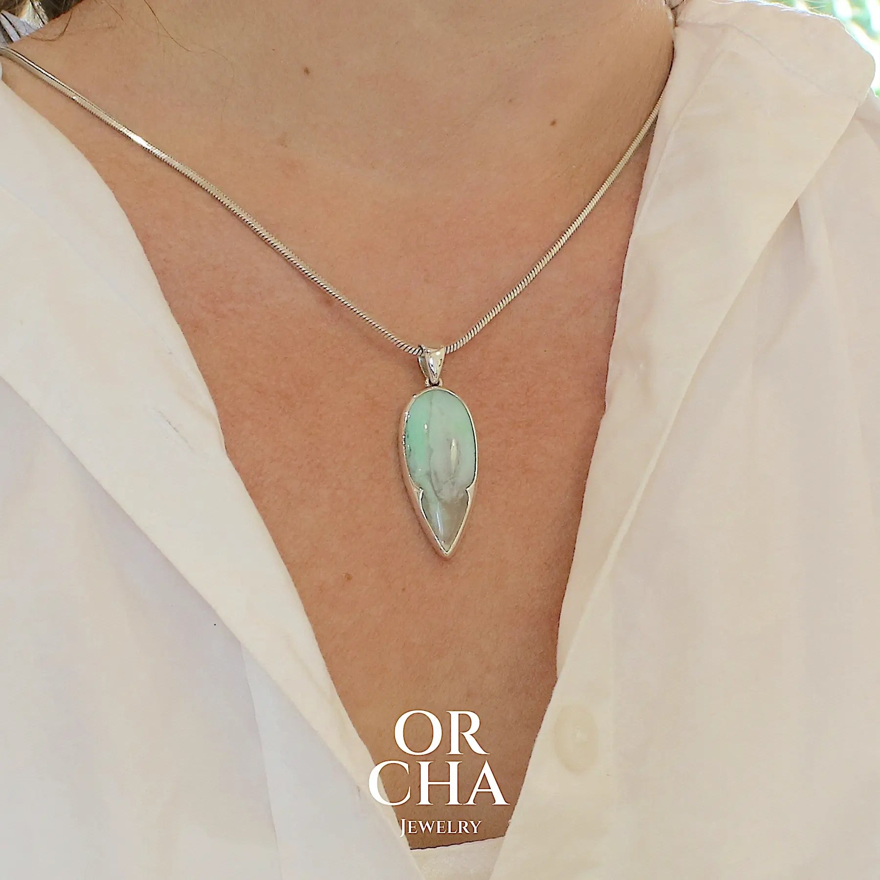 photo sur modèle d'un pendentif pour femme et homme en argent massif, sertie d'un cabochon d'opale bleue du Pérou de couleur verte bleutée. Pierre en forme de goutte inversée. Pierre opaque et translucide. Bijoux unique, éthique et durable présenté dans un coffret de notre marque, prêt à offrir. Livraison offerte, certificat d'authenticité, service client.
