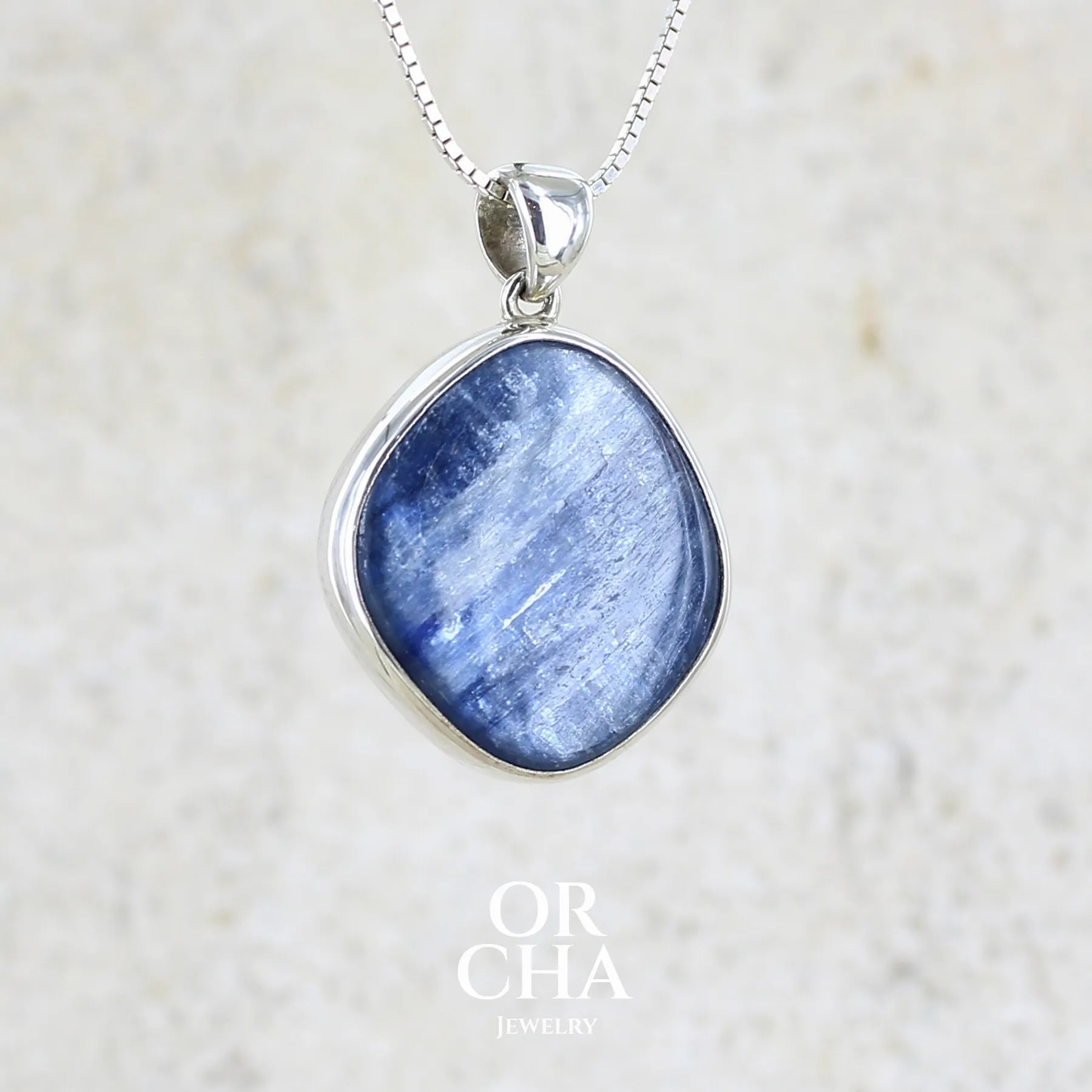 Pendentif en argent massif serti d'un cabochon de cyanite de couleur bleue jeans nacré. Pierre de qualité opaque comportant des inclusions. Bijoux unique par Orcha Jewelry