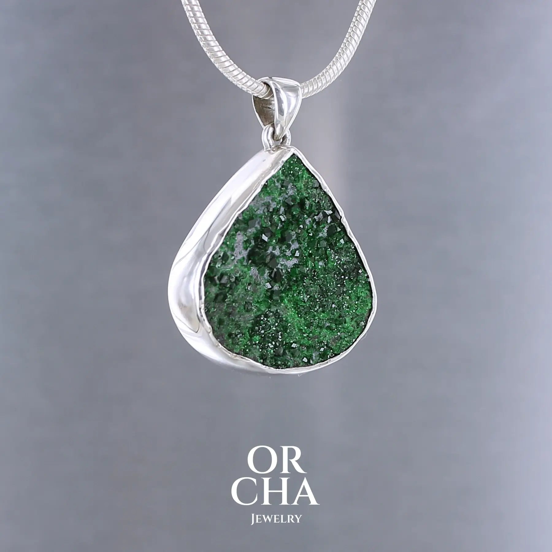 Pendentif en argent massif serti d'une Uvarovite brute ( variété de Grenat ). Pierre brute recouverte de cristaux scintillants de couleur verte, taillée en forme de goutte. Bijoux unique, éthique et durable présenté dans un coffret de notre marque, prêt à offrir. Livraison offerte, certificat d'authenticité, service client.
