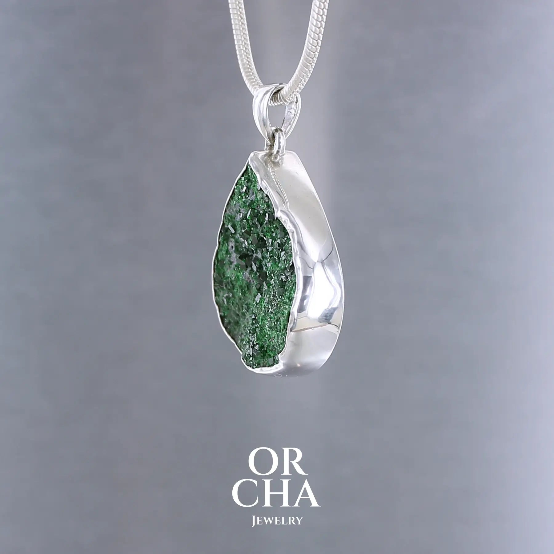 Pendentif en argent massif serti d'une Uvarovite brute ( variété de Grenat ). Pierre brute recouverte de cristaux scintillants de couleur verte, taillée en forme de goutte. Bijoux unique, éthique et durable présenté dans un coffret de notre marque, prêt à offrir. Livraison offerte, certificat d'authenticité, service client.
