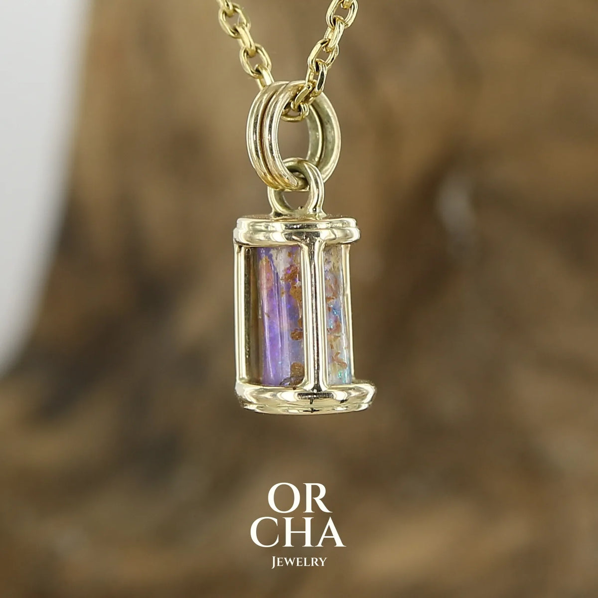 Pendentif pour femme en or jaune massif 14k serti d'une opale pipe aux feux  multicolores à dominantes bleu et violet. Specimen cylindrique, sertissage cage, opale rarement proposé en bijouterie. Bijou unique par par Orchajewelry