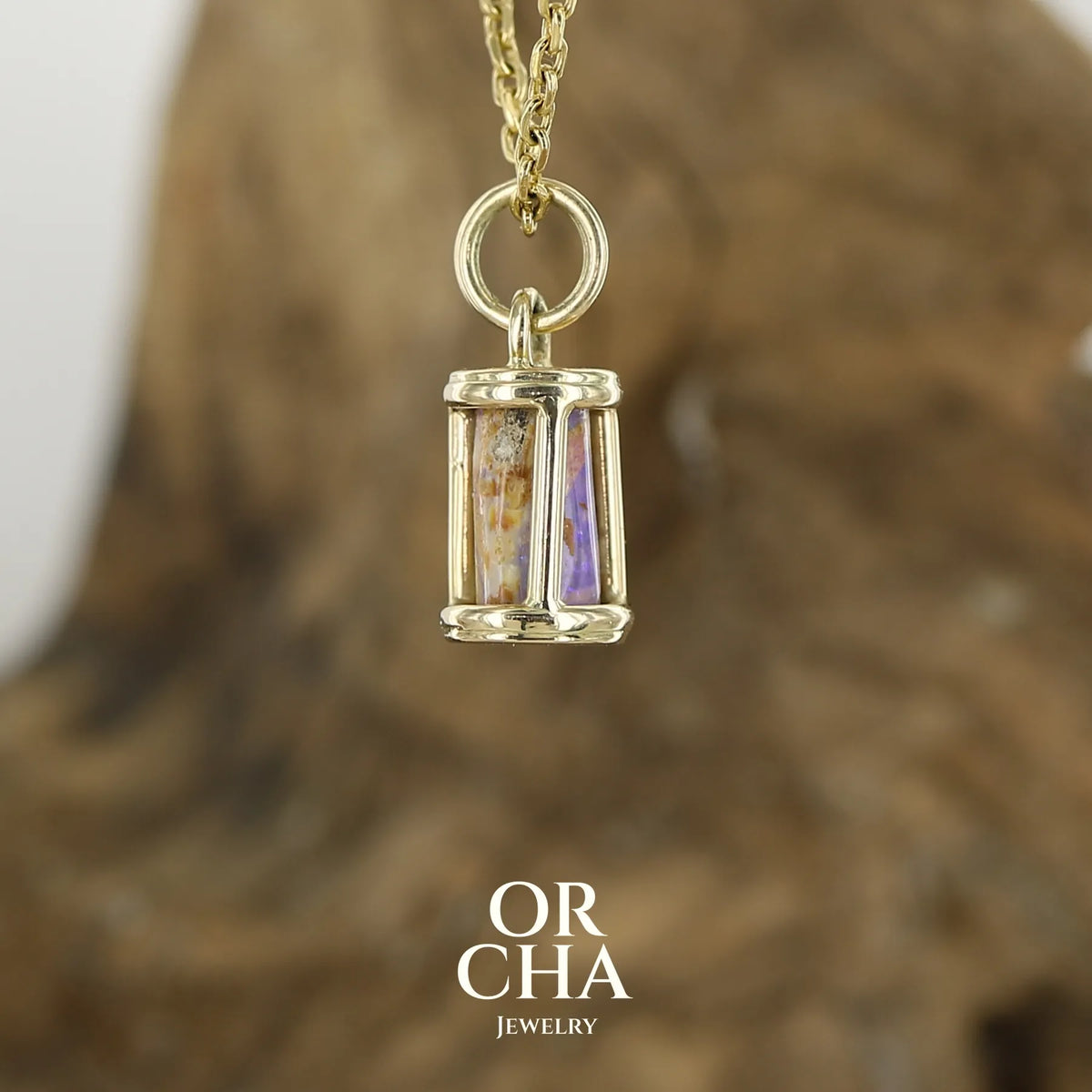 Profil d'une pendentif pour femme en or jaune massif 14k serti d'une opale pipe aux feux  multicolores à dominantes bleu et violet. Specimen cylindrique, sertissage cage, opale rarement proposé en bijouterie. Bijou unique par par Orchajewelry