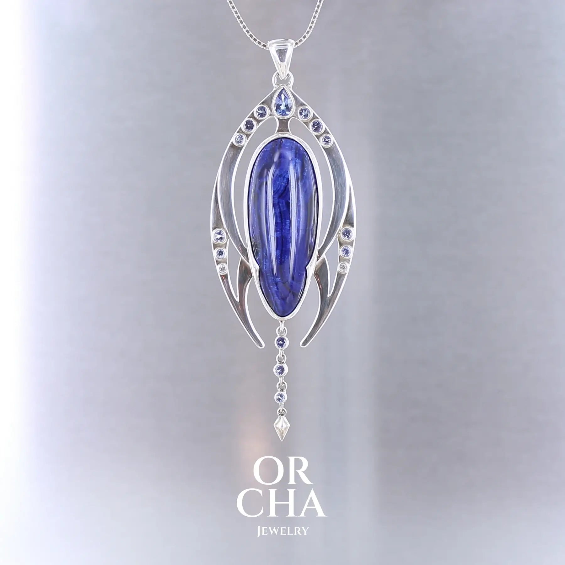 Pendentif contemporain en argent massif représentant une forme organique stylisée. Il est orné d’une azurite bleu profond de forme ovale allongée, encadrée de deux structures symétriques serties de petites tanzanite rondes violettes. Une ligne de pierres descend sous la pierre centrale, se terminant par un élément pointu sculpté. Bijoux unique, éthique et durable présenté dans un coffret de notre marque, prêt à offrir. Livraison offerte, certificat d'authenticité, service client.