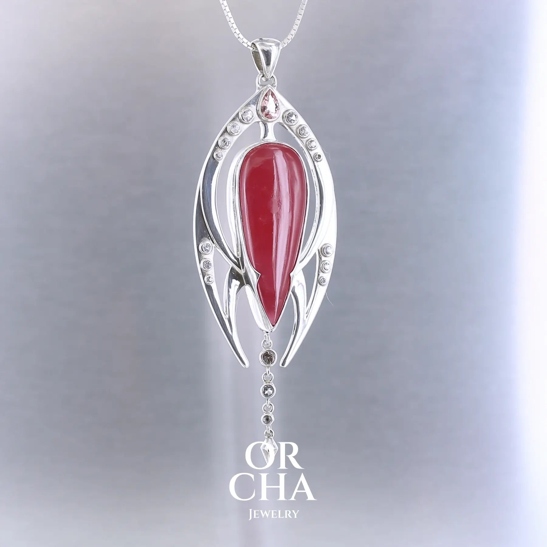 Pendentif exclusif, création originale, pour femme en argent massif serti d'une Rhodonite de très belle qualité, d'une tourmaline et de goshénite. Pierre de couleur rouge coquelicot, rose pastel et blanche, translucide à transparentes. Pierre naturelle, en forme de goutte, taillée en cabochon. Bijoux unique, éthique et durable présenté dans un coffret de notre marque, prêt à offrir. Livraison offerte, certificat d'authenticité, service client