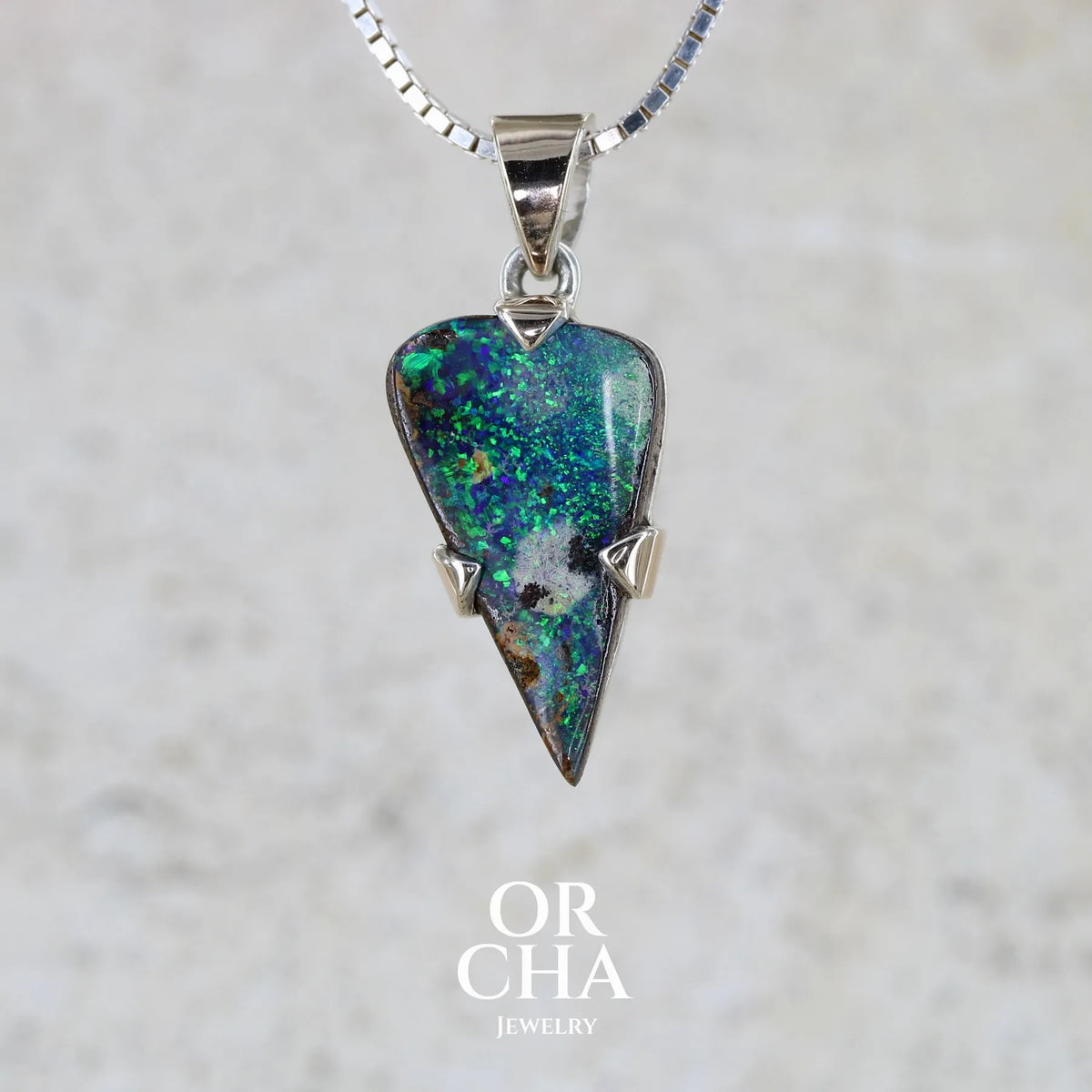 Pendentif pour homme en or 9k et argent massif 925 serti d'une opale boulder aux feux multicolores bleus et verts. Tranche d'opale massive naturelle taillée en forme d'aile. Pierre de qualité opaque originaire d'Australie. Bijoux unique par Orcha Jewelry.