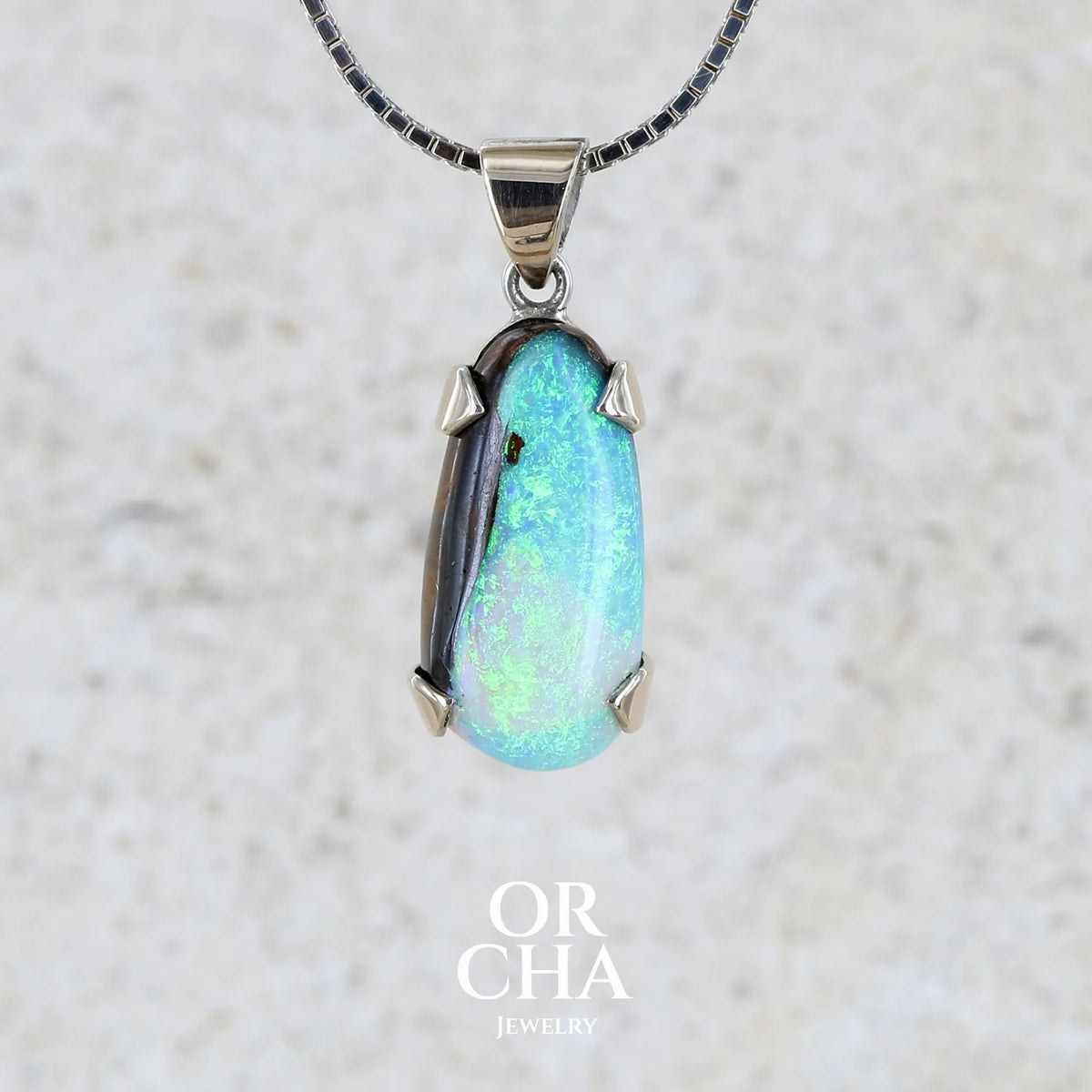 Pendentif pour femme en or 9k et argent massif serti d'une opale boulder cristal aux feux étoilés multicolores à dominantes bleu turquoise. Cabochon de 7 carat taillé en forme de goutte de qualité translucide. Opale massive australienne. Bijou unique réalisé par Orchajewelry