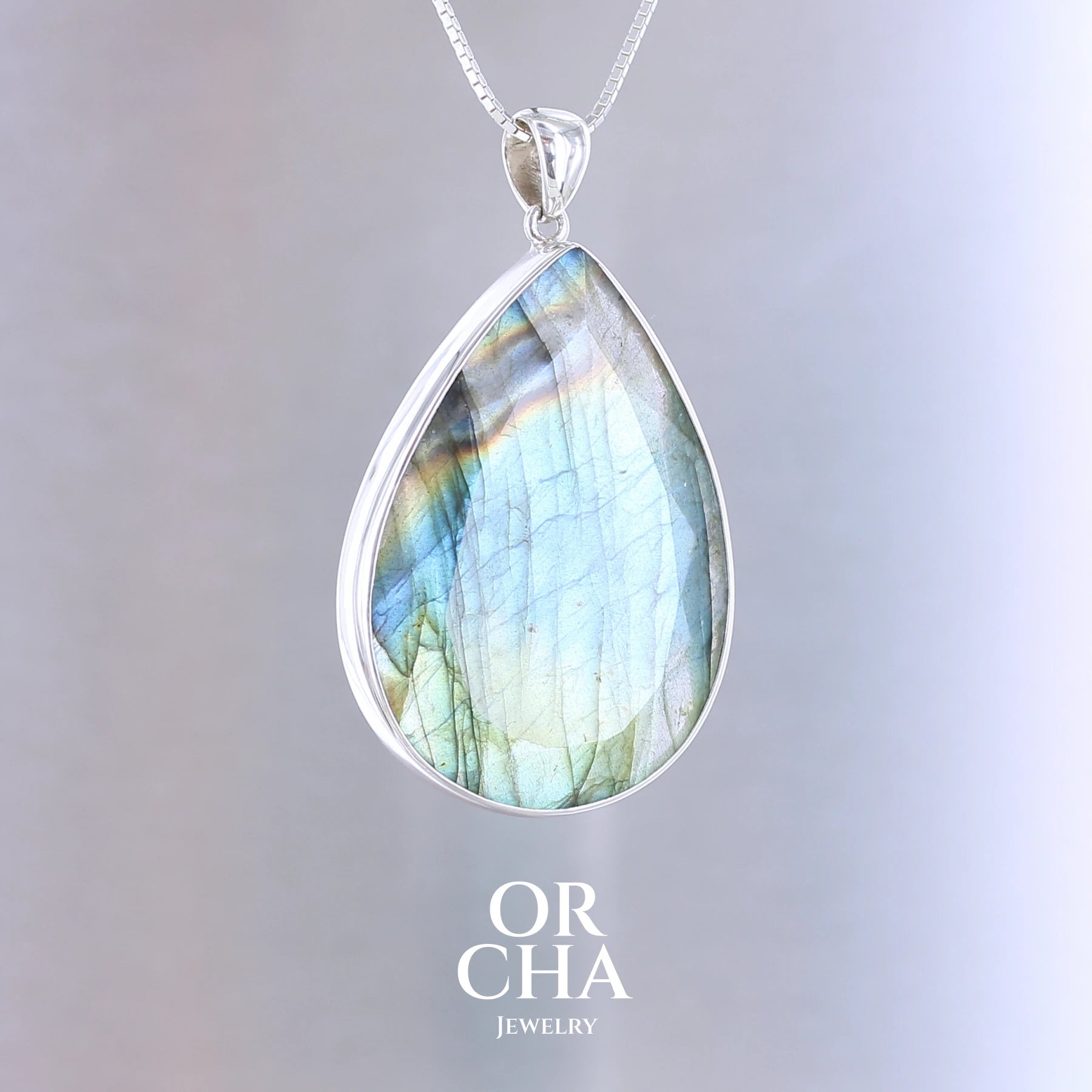 Pendentif pour femme en argent massif sertie d'une labradorite aux reflets bleus, bronzes et multicolores selon la lumière. Pierre facettée naturelle translucide présentant des inclusions fréquents sur ce type de pierre. Bijoux unique, éthique et durable présenté dans un coffret de notre marque, prêt à offrir. Livraison offerte, certificat d'authenticité, service client.