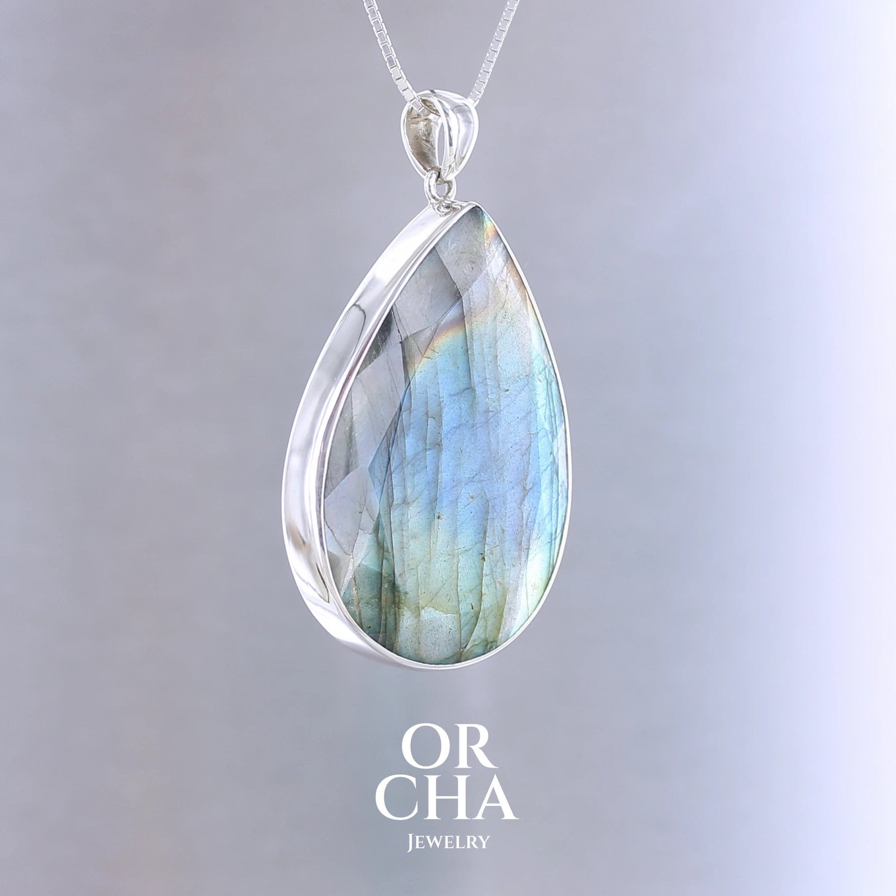 Pendentif pour femme en argent massif sertie d'une labradorite aux reflets bleus, bronzes et multicolores selon la lumière. Pierre facettée naturelle translucide présentant des inclusions fréquents sur ce type de pierre. Bijoux unique, éthique et durable présenté dans un coffret de notre marque, prêt à offrir. Livraison offerte, certificat d'authenticité, service client.