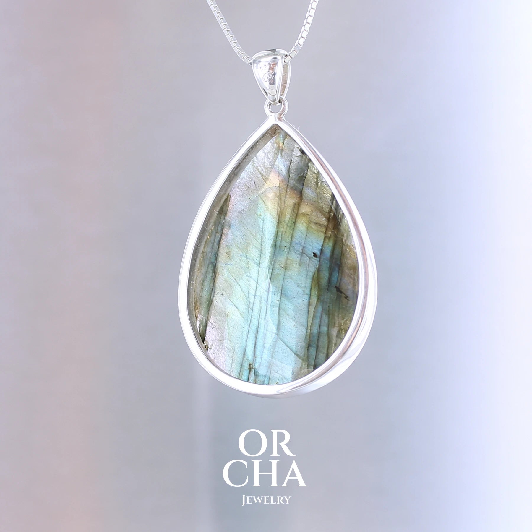 Pendentif pour femme en argent massif sertie d'une labradorite aux reflets bleus, bronzes et multicolores selon la lumière. Pierre facettée naturelle translucide présentant des inclusions fréquents sur ce type de pierre. Bijoux unique, éthique et durable présenté dans un coffret de notre marque, prêt à offrir. Livraison offerte, certificat d'authenticité, service client.