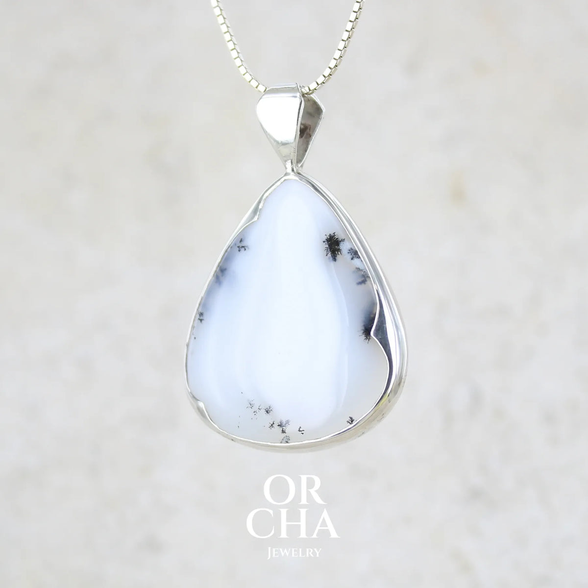 Pendentif pour femme en argent massif sertie d'un cabochon en forme de goutte  d'agate dendritique de couleur blanc pur et noir. Pierre opaque à translucide à inclusions paysages de dendrites de manganèse noires contrastées. Bijou unique réalisé par Orchajewelry