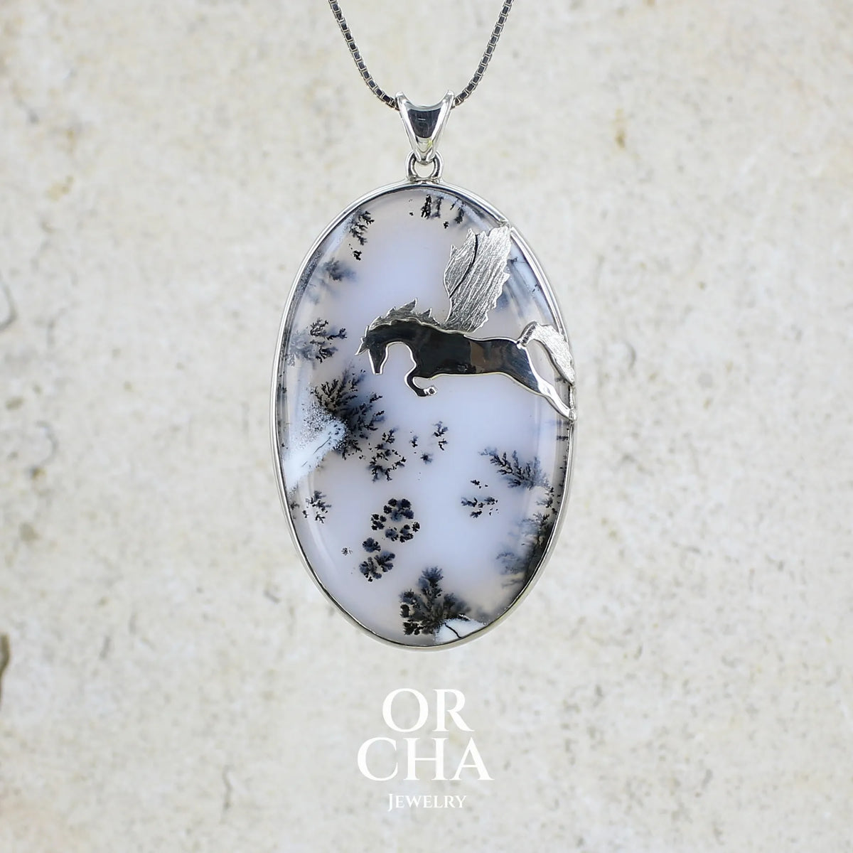 Pendentif en argent massif sertie d'un grand cabochon de forme ovale d'agate dendritique de couleur blanc pur et noir. Pierre opaque à translucide à inclusions paysages de dendrites de manganèse noires contrastées. Bijou unique illustré d'un cheval ailé réalisé par Orchajewelry