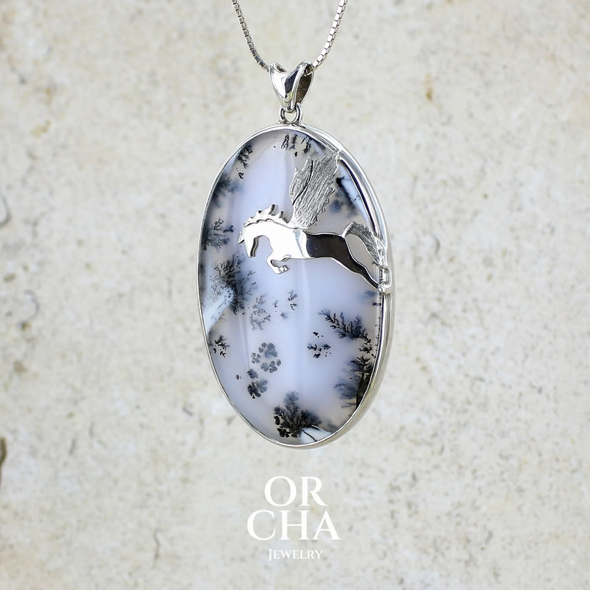Pendentif en argent massif sertie d'un grand cabochon de forme ovale d'agate dendritique de couleur blanc pur et noir. Pierre opaque à translucide à inclusions paysages de dendrites de manganèse noires contrastées. Bijou unique illustré d'un cheval ailé réalisé par Orchajewelry